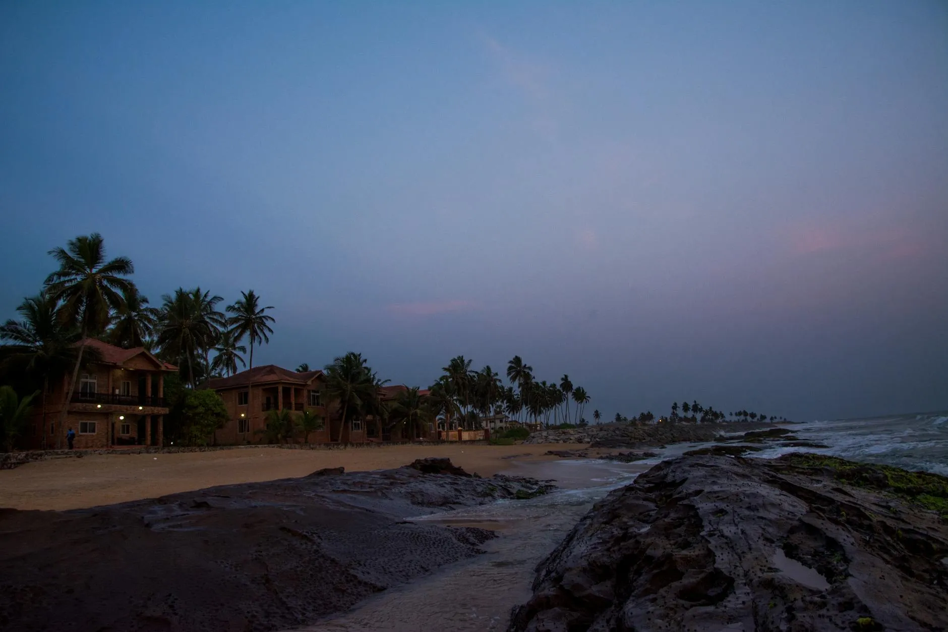 Tranquil Elmina beach at dusk with palm trees and rocky shore in Ghana.