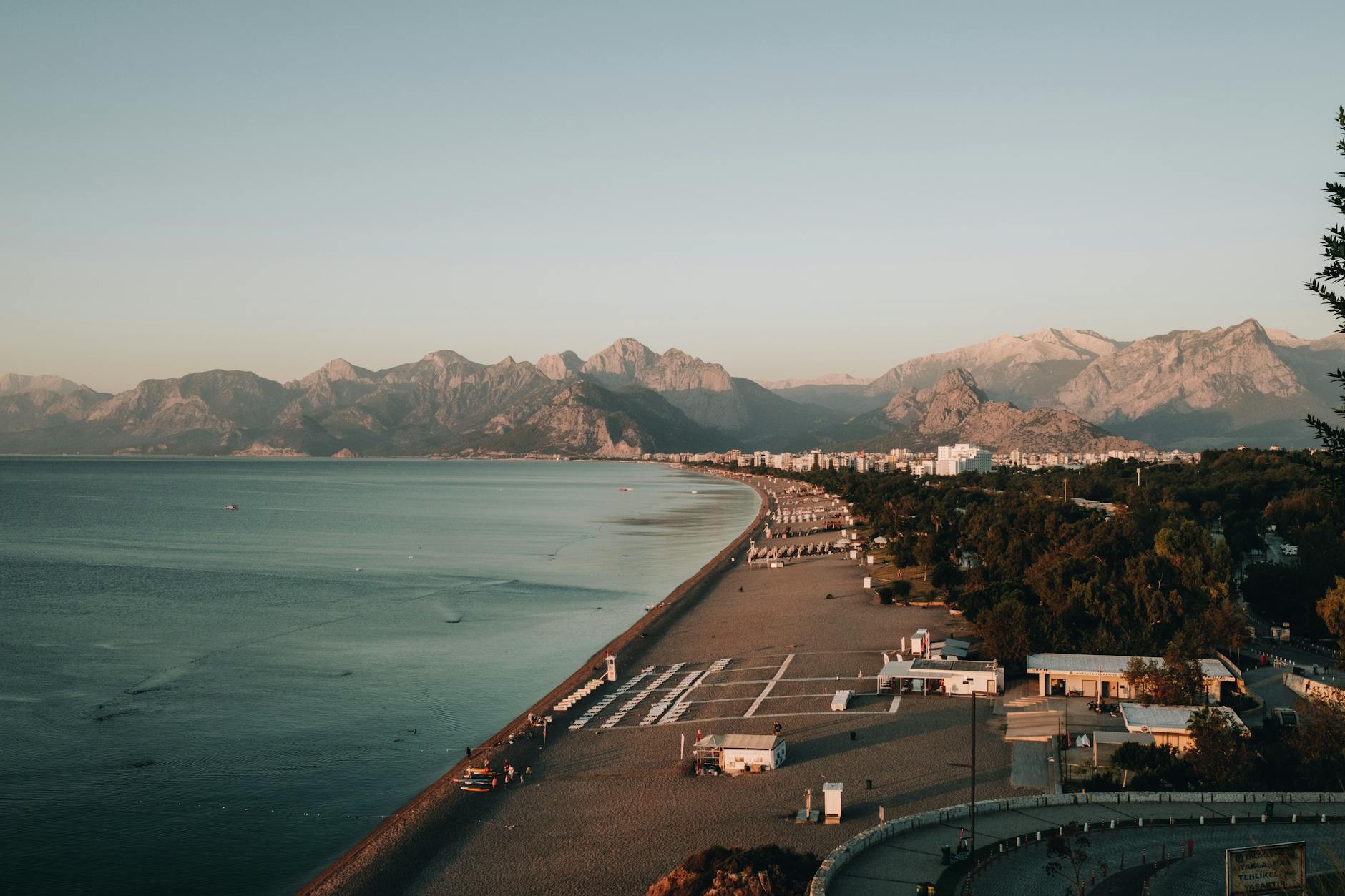 Explore Antalya's beautiful coastline with mountains, beach, and resort town at dawn.