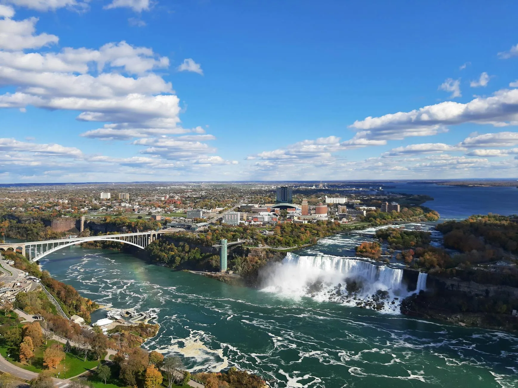 Buffalo / Niagara — Stunning aerial shot of Niagara Falls and Rainbow Bridge with vibrant autumn scenery.
