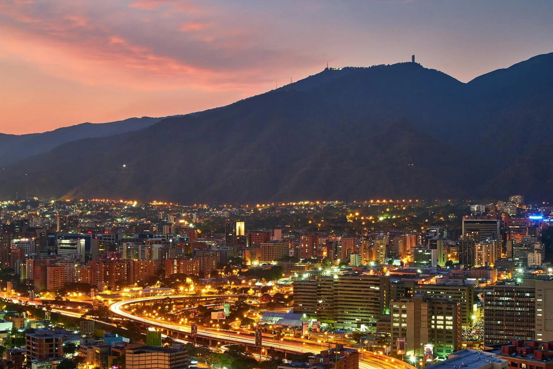 Caracas, Venezuela — A stunning aerial view of Caracas cityscape at dusk, showcasing the vibrant city lights against the mountainous backdrop.