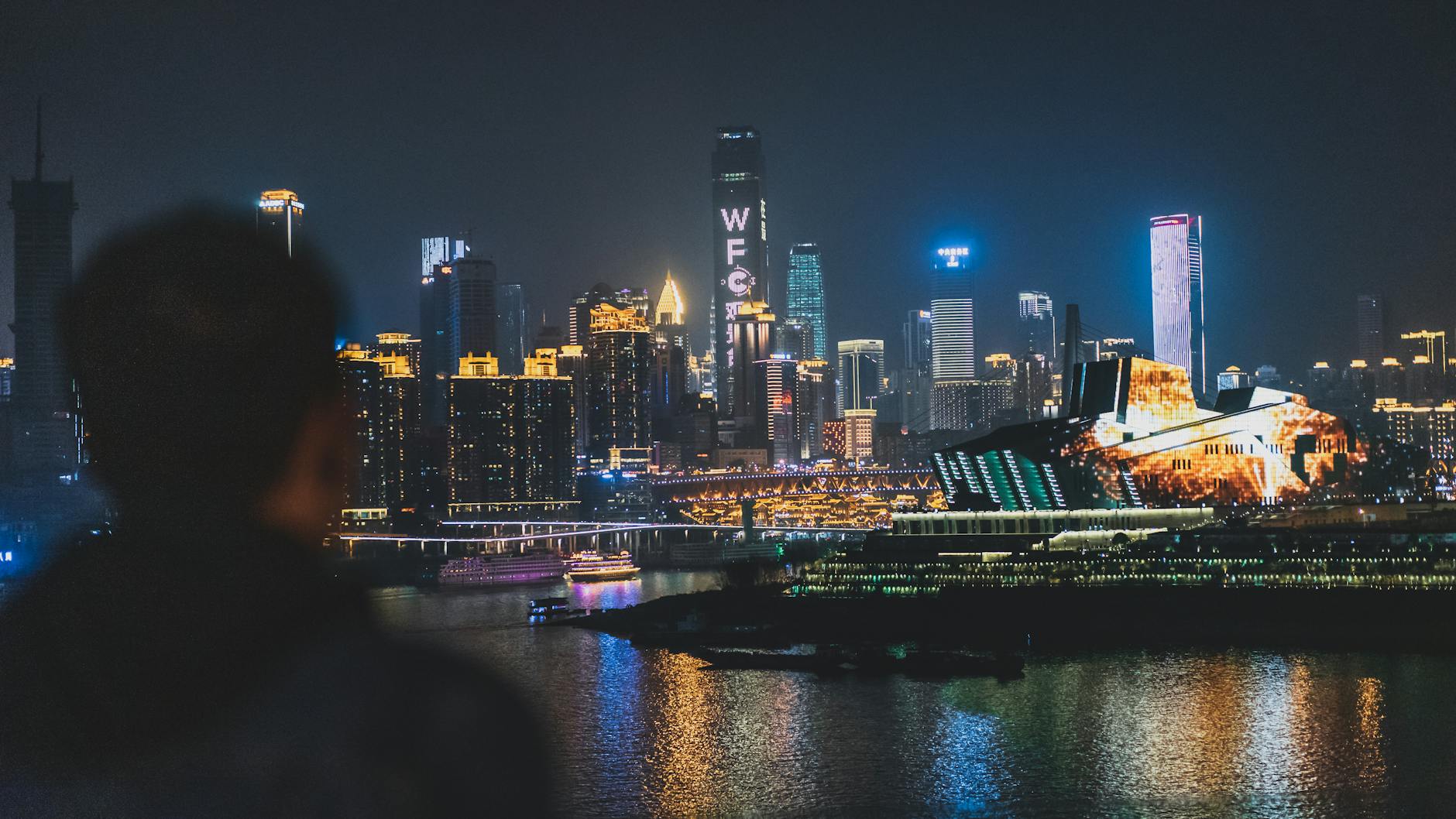 Chongqing Jiangbei International Airport (CKG) — Back view unrecognizable blurred male enjoying amazing view of contemporary illuminated embankment in Chungking China during night
