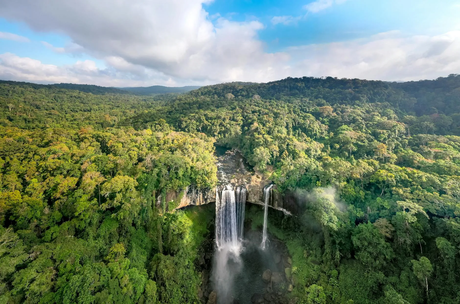 Guinea — A breathtaking aerial view of a lush rainforest featuring a stunning waterfall cascading into a river.