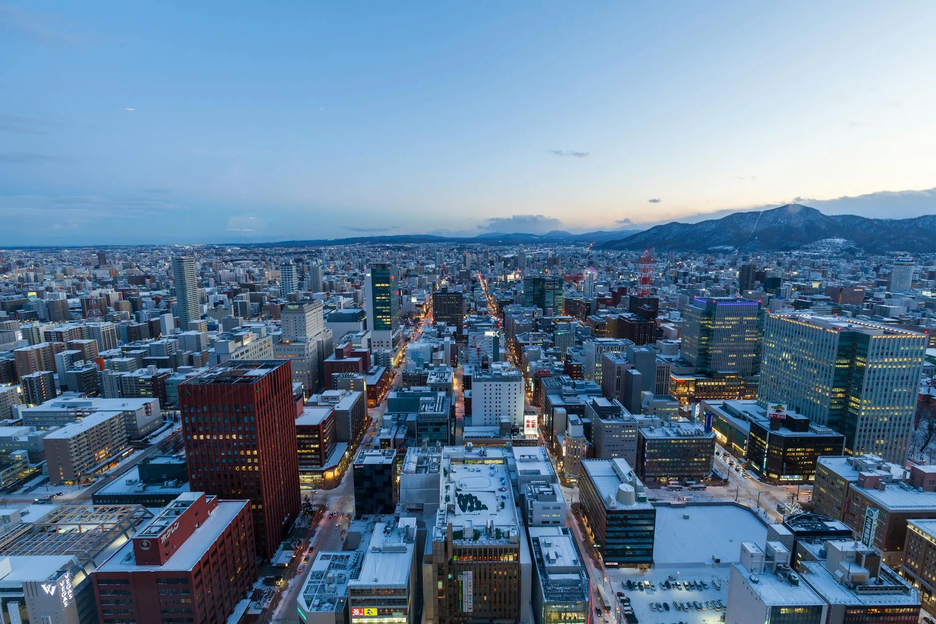 Sapporo, Hokkaido, Japan — Captivating aerial view of Sapporo, Japan in winter at dusk with snow-covered buildings and distant mountains.