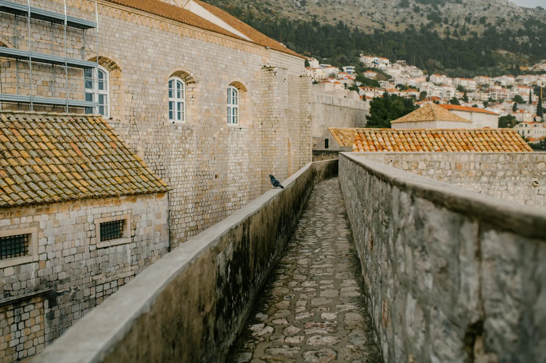 Old stone structure with narrow pathway and fence near brick houses in city on hills