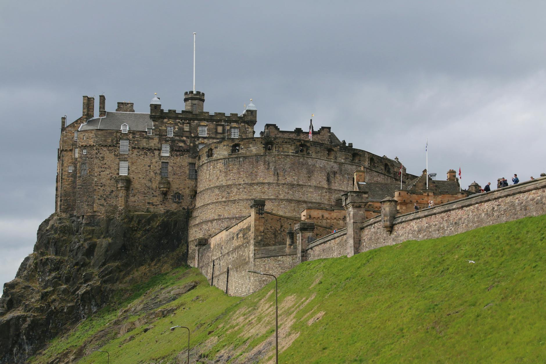 View of Edinburgh Castle perched on a historic rock with a cloudy sky. Iconic Scottish landmark.