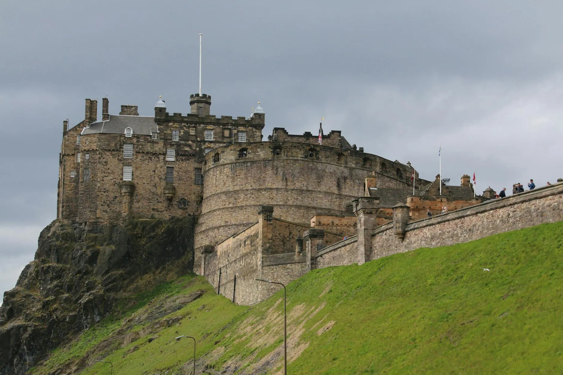 View of Edinburgh Castle perched on a historic rock with a cloudy sky. Iconic Scottish landmark.