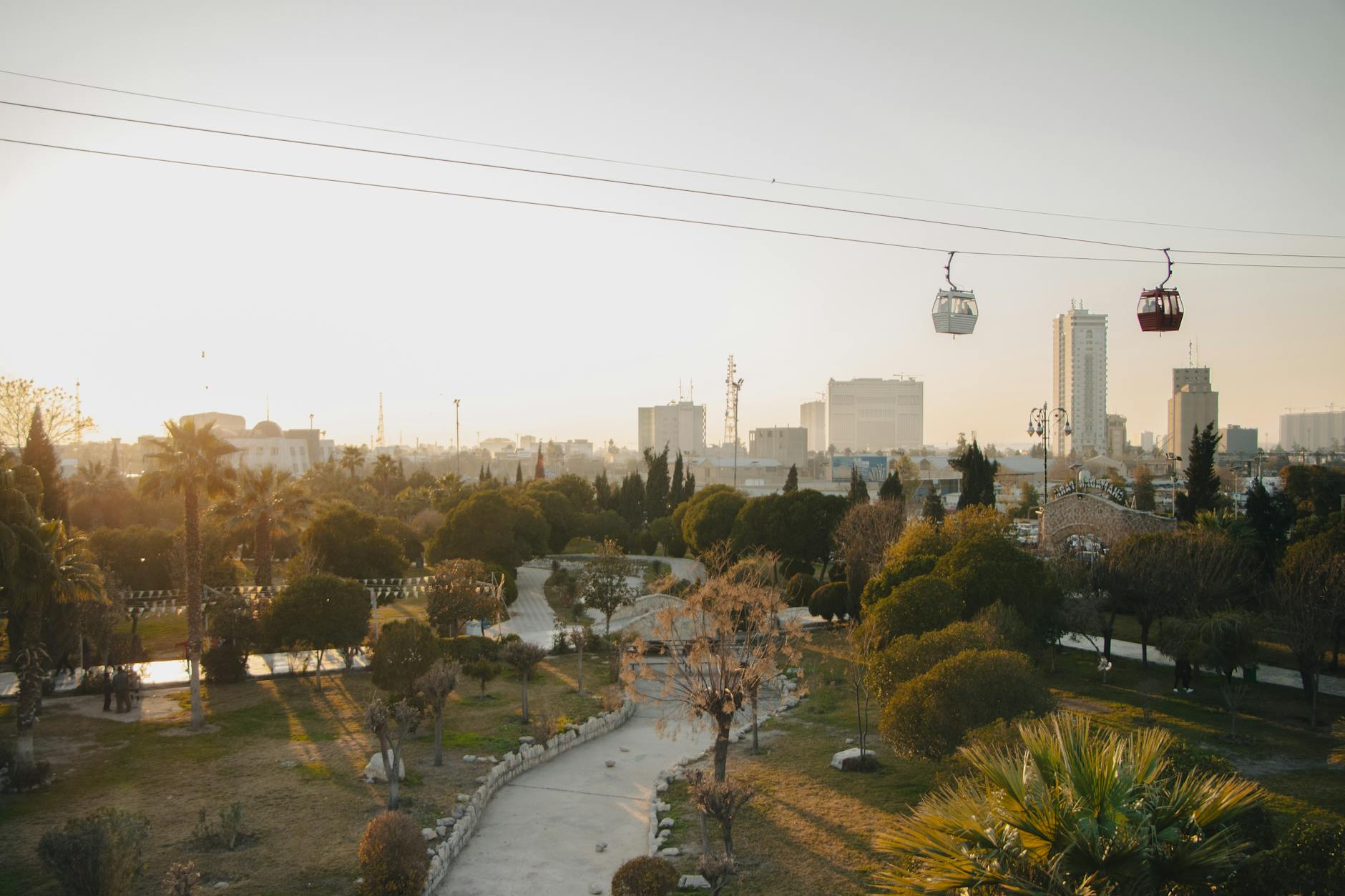 Stunning aerial view of a park in Erbil, Iraq with cable cars and the city skyline at sunset.