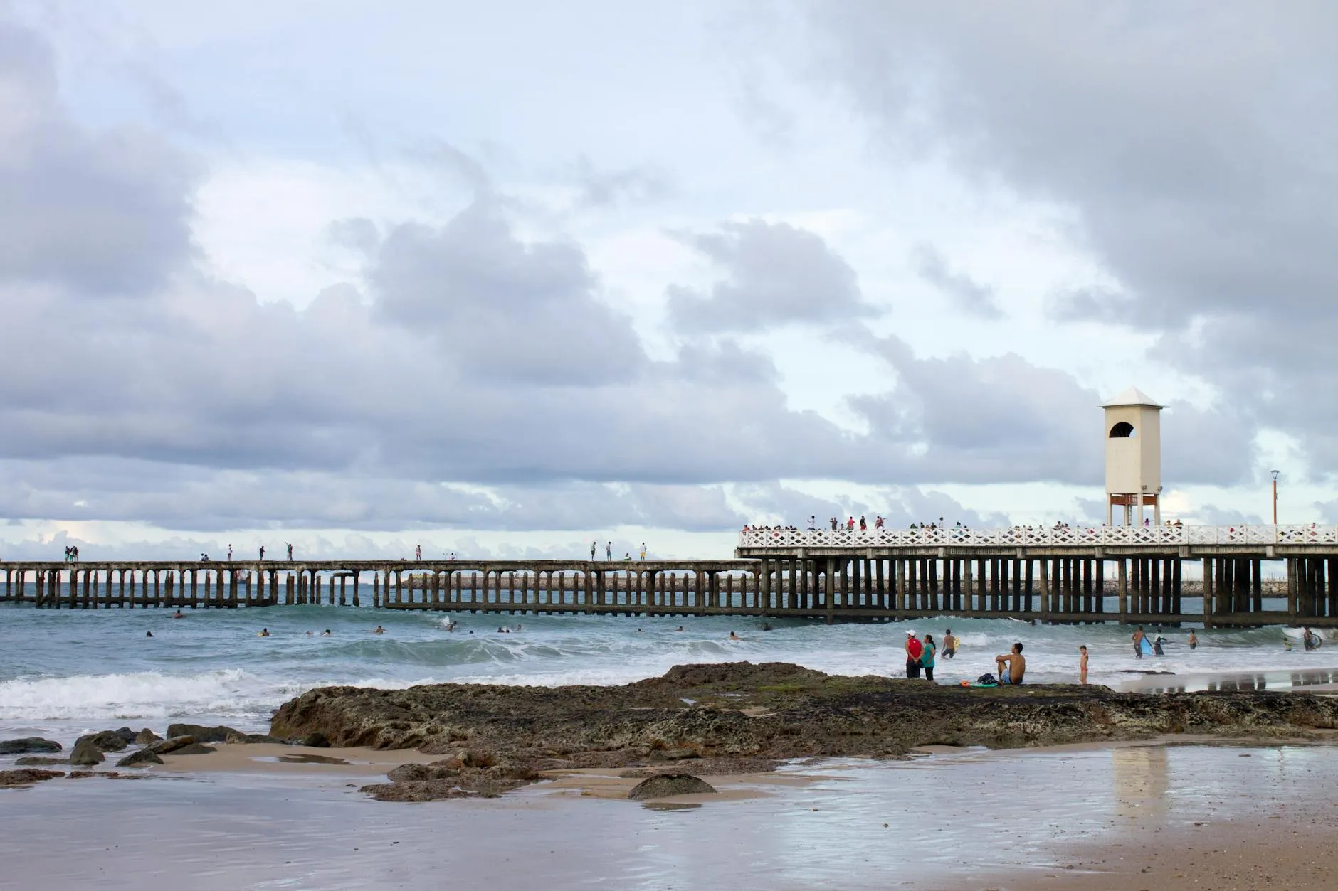A scenic view of a beach with a pier and cloudy sky at Praia de Iracema, Fortaleza, Brazil.