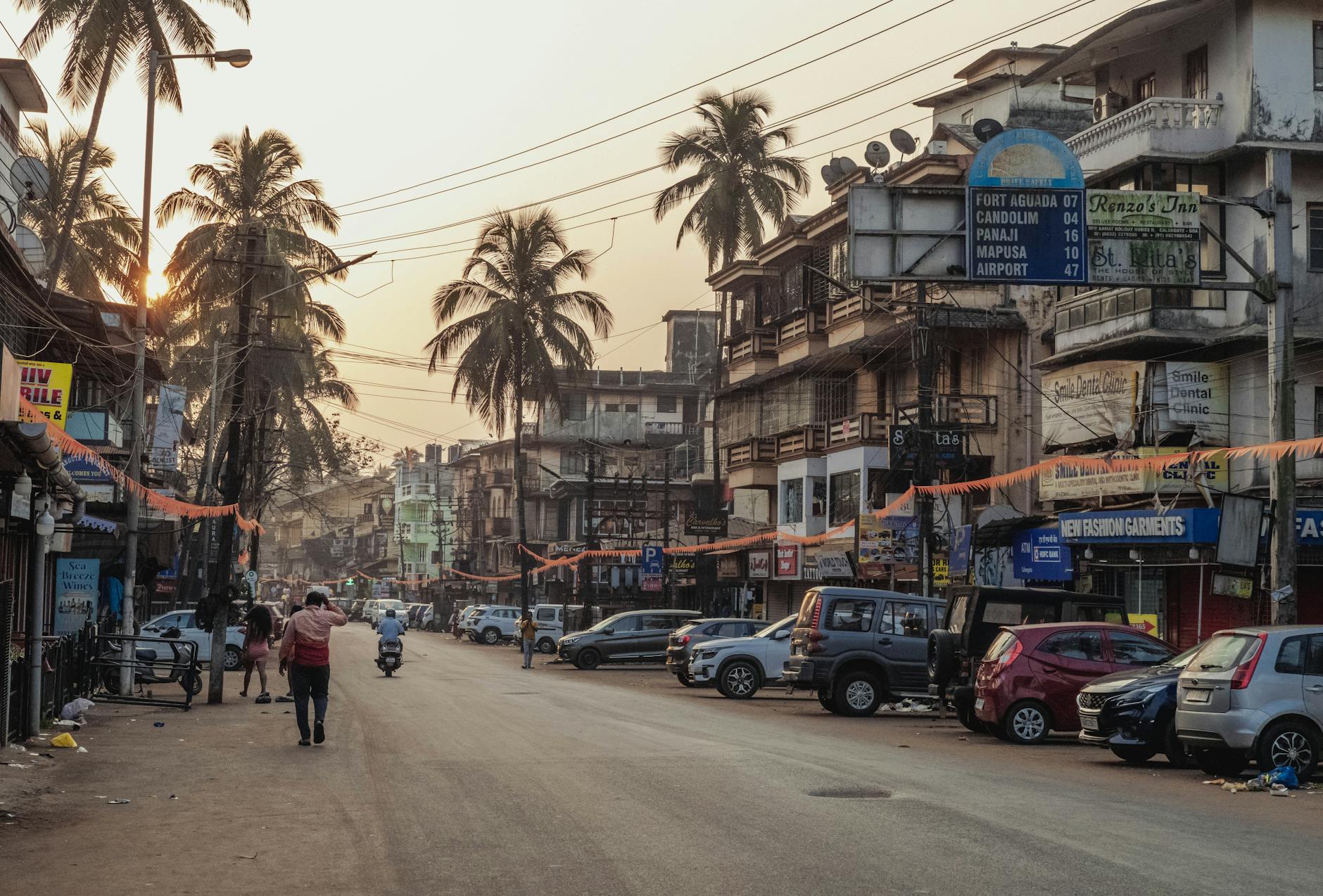 Street scene at sunset in Calangute, India with palm trees and local shops.