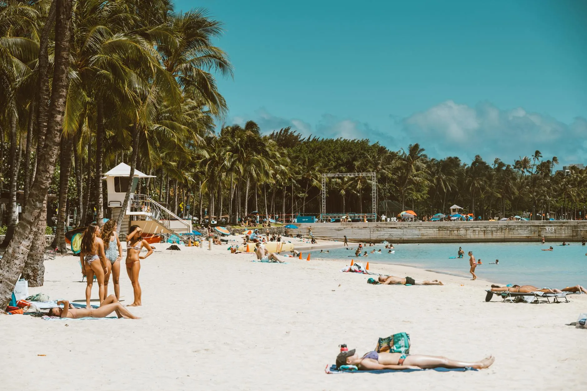 Daniel K. Inouye International Airport (HNL) — Relaxing beach scene with sunbathers and palm trees under a bright blue sky, ideal vacation setting.