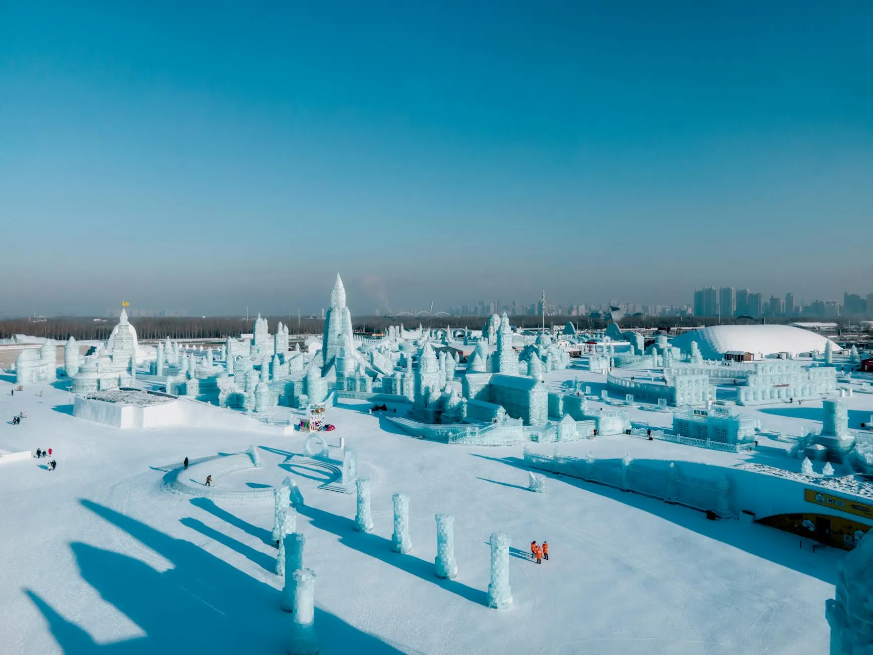 Harbin, China — Stunning aerial view of Harbin Ice and Snow Festival with intricate ice sculptures under a clear blue sky.