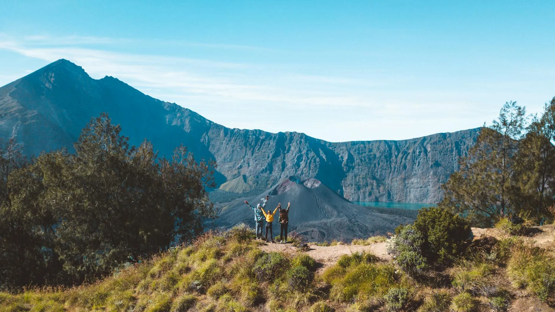 Lombok, Indonesia — Three hikers raise their arms in joy at the crater rim of Mount Rinjani, Lombok, Indonesia.