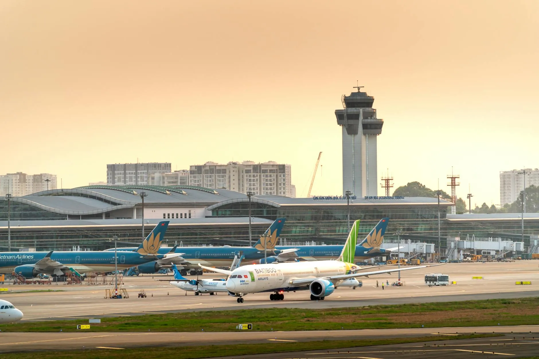 Airplanes parked on a runway under a dramatic golden sunset sky at a modern airport terminal.