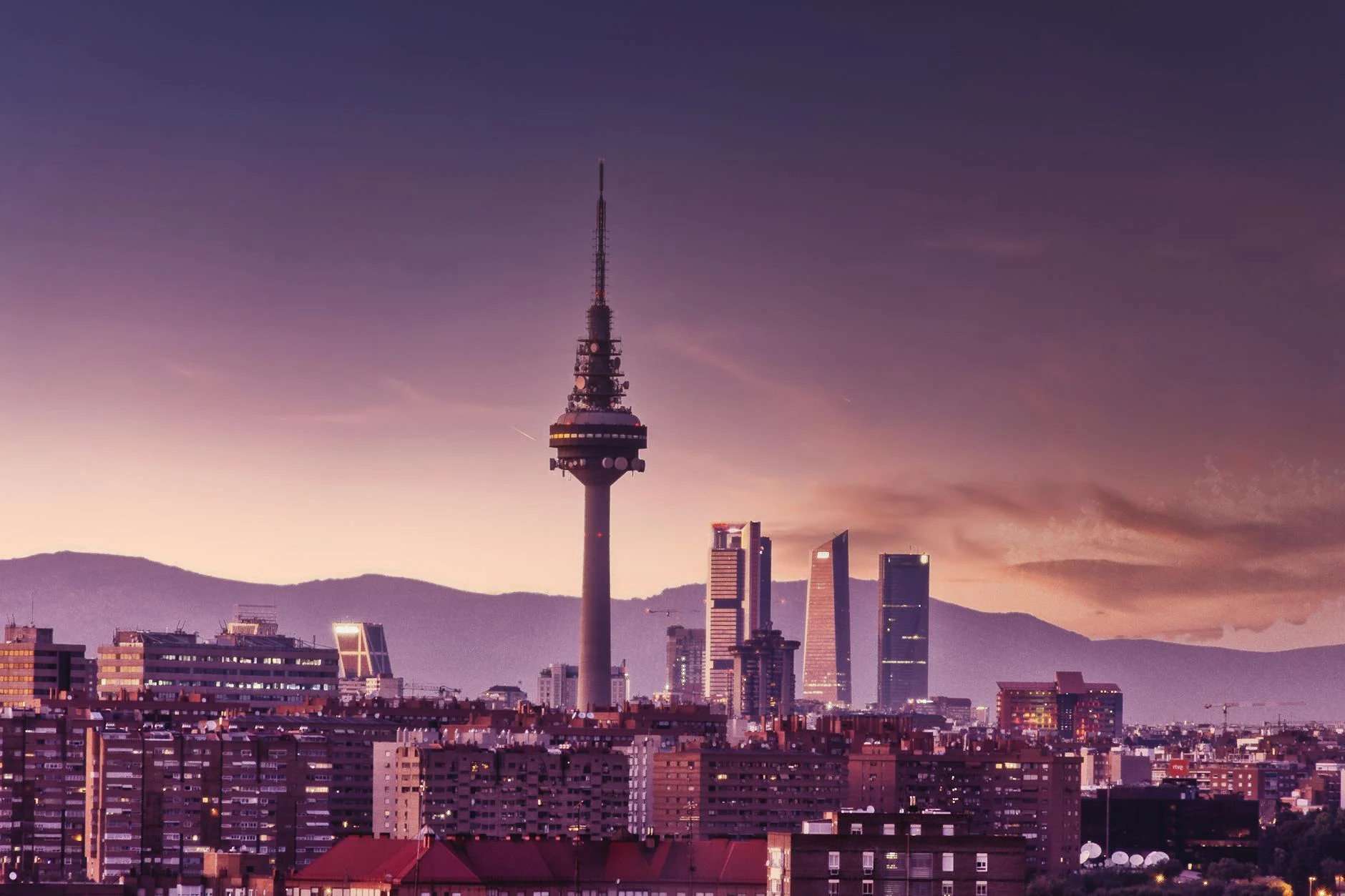 Stunning view of Madrid's skyline at twilight featuring the iconic Torrespaña Tower and mountains in the background.