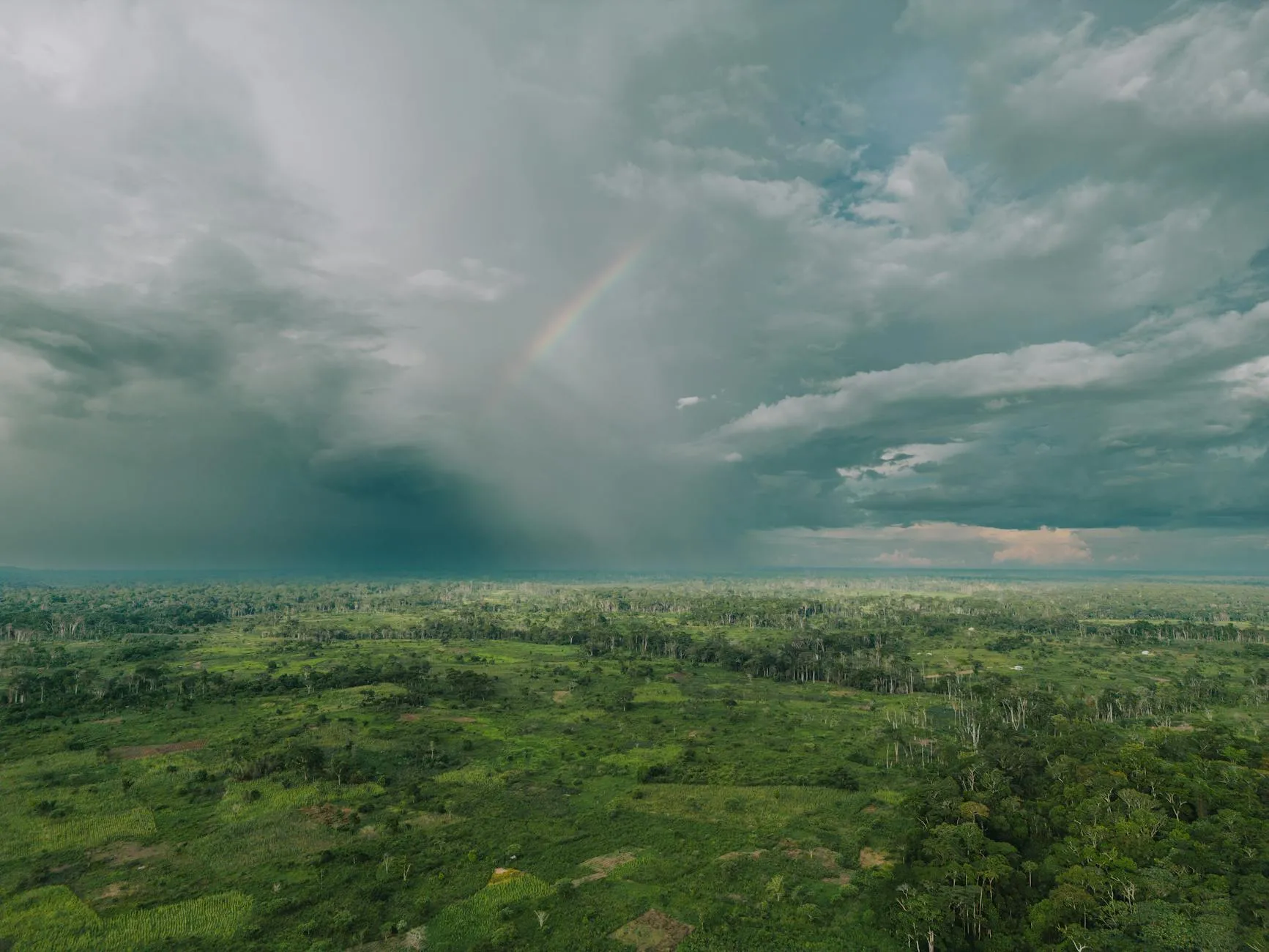 Explore the lush Cameroon rainforest from above, capturing a rainbow amidst dramatic clouds.