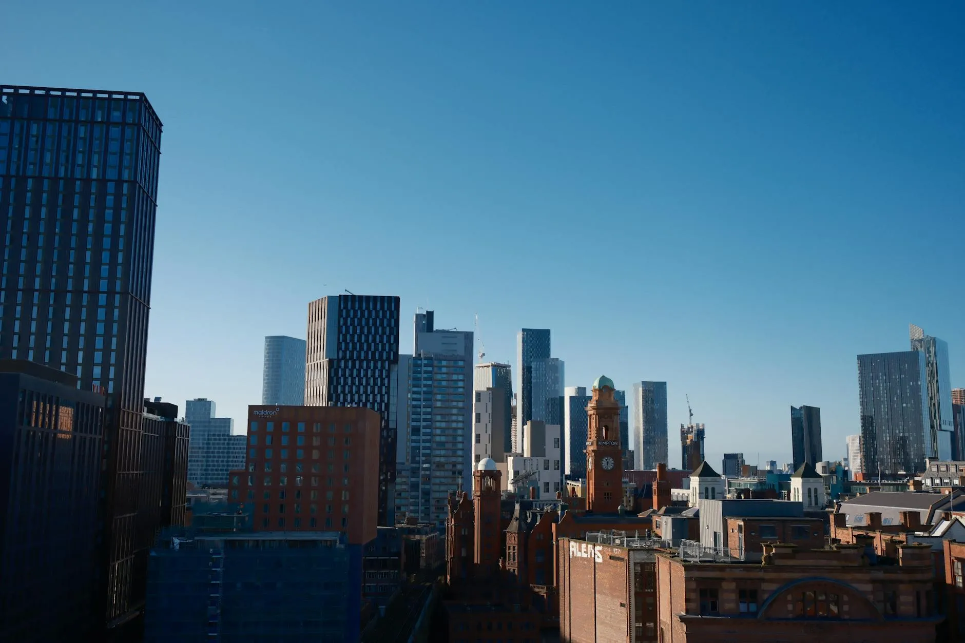 Skyline of Manchester city featuring the iconic Beetham Tower under a bright blue sky.