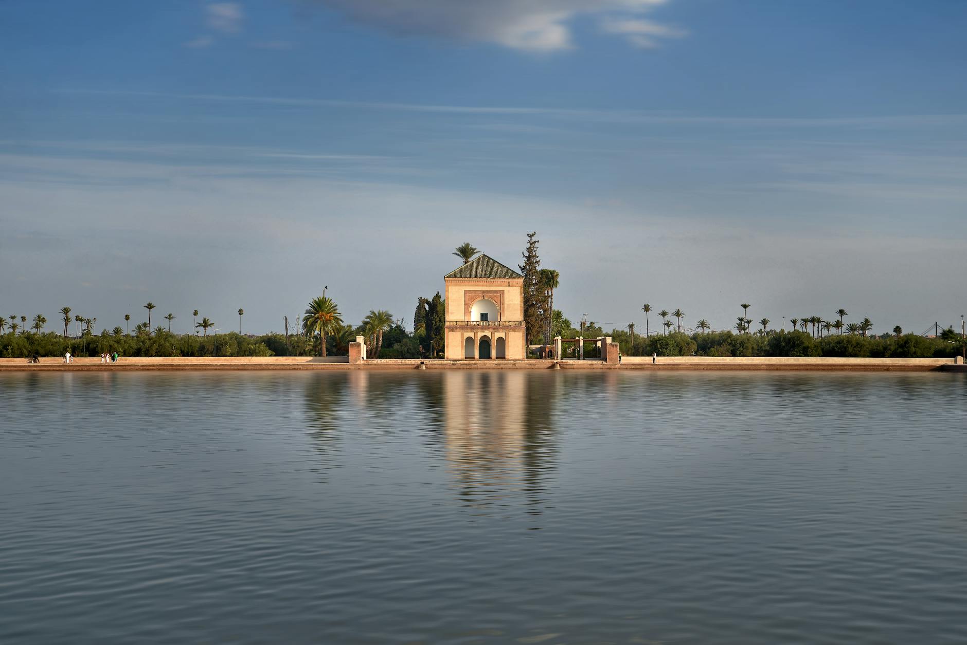 Tranquil view of Menara Gardens pavilion reflecting in water under a clear blue sky in Marrakech.