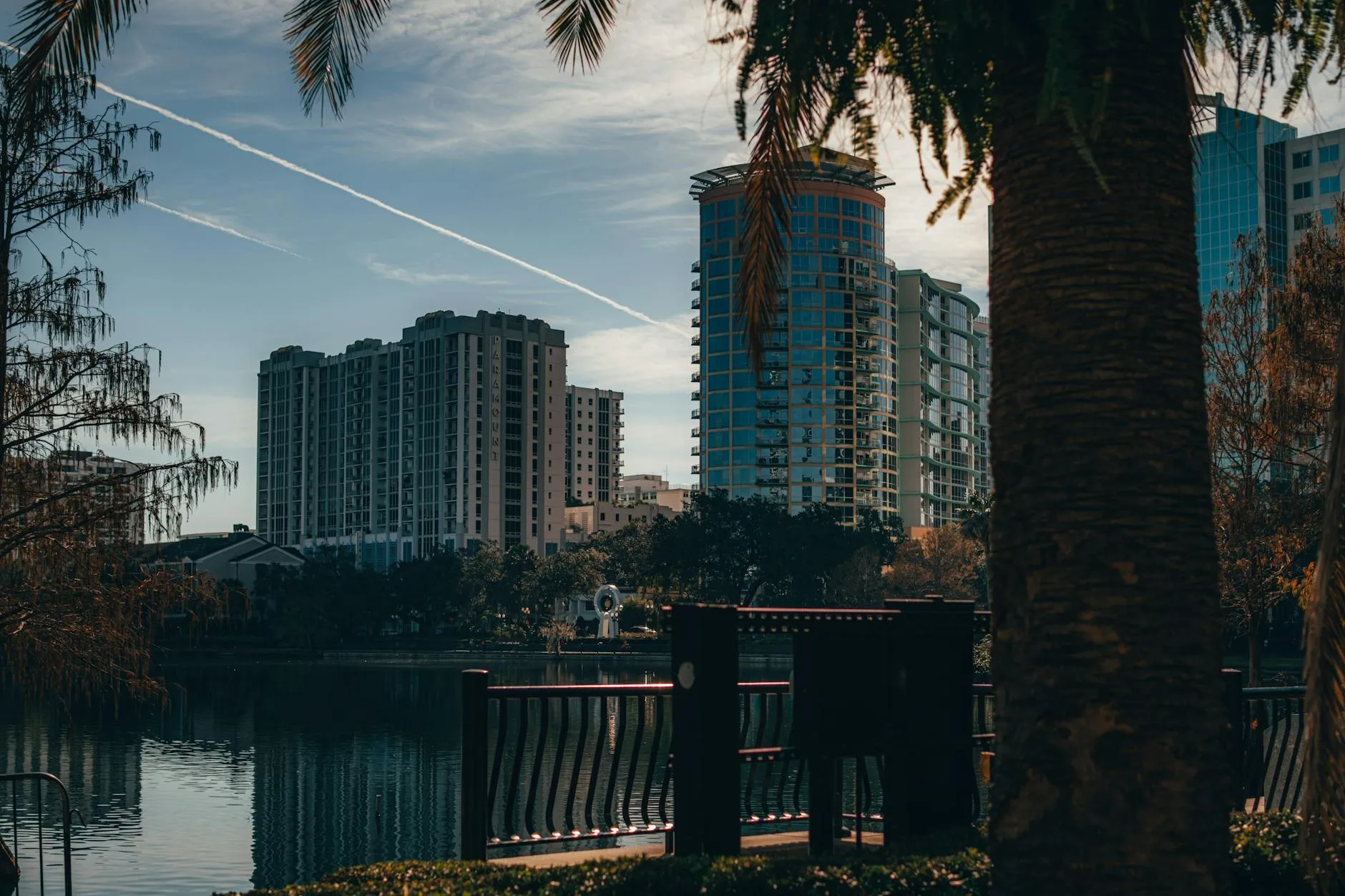Orlando International Airport (MCO) — View of Orlando's modern skyline reflecting on a tranquil lake, surrounded by trees.