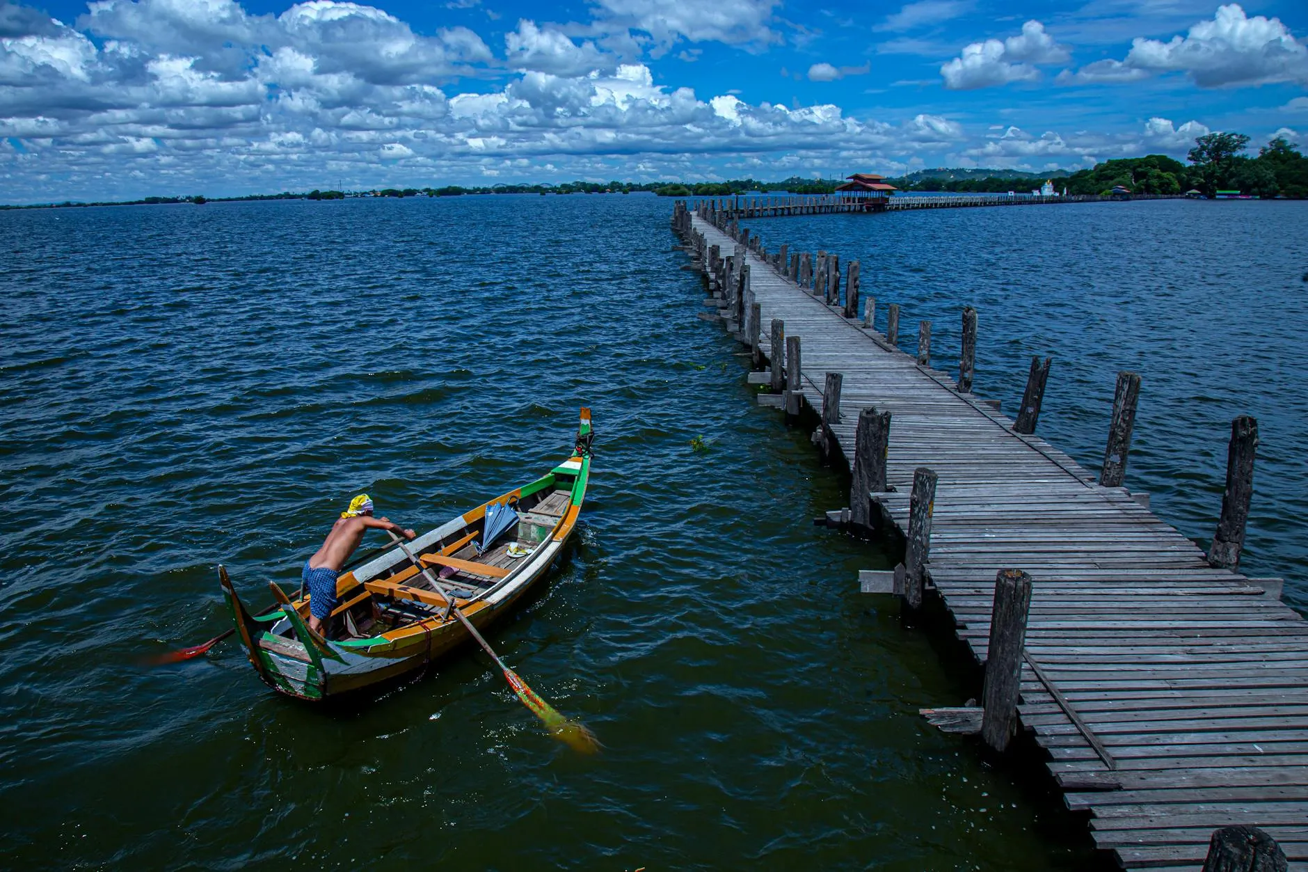 Mandalay, Myanmar — A person rows a traditional boat on Taungthaman Lake beside U Bein Bridge, Mandalay, Myanmar.
