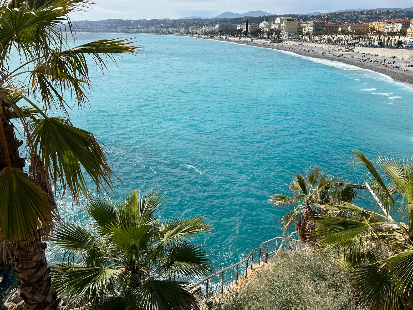 Aerial view of the beautiful coastline and vibrant city of Nice, France, with palm trees and turquoise sea.