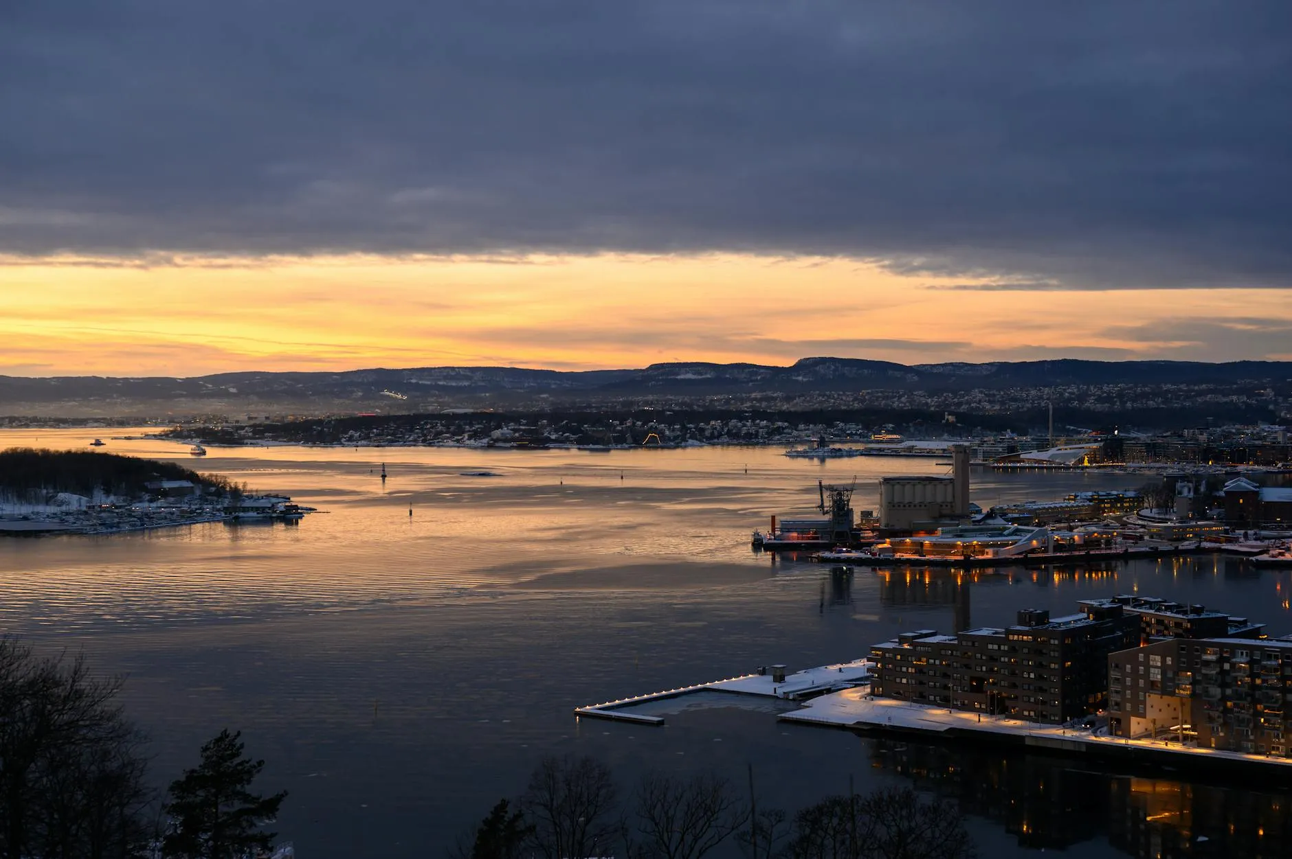 Aerial sunset view of Oslo Fjord with city skyline and dramatic clouds.