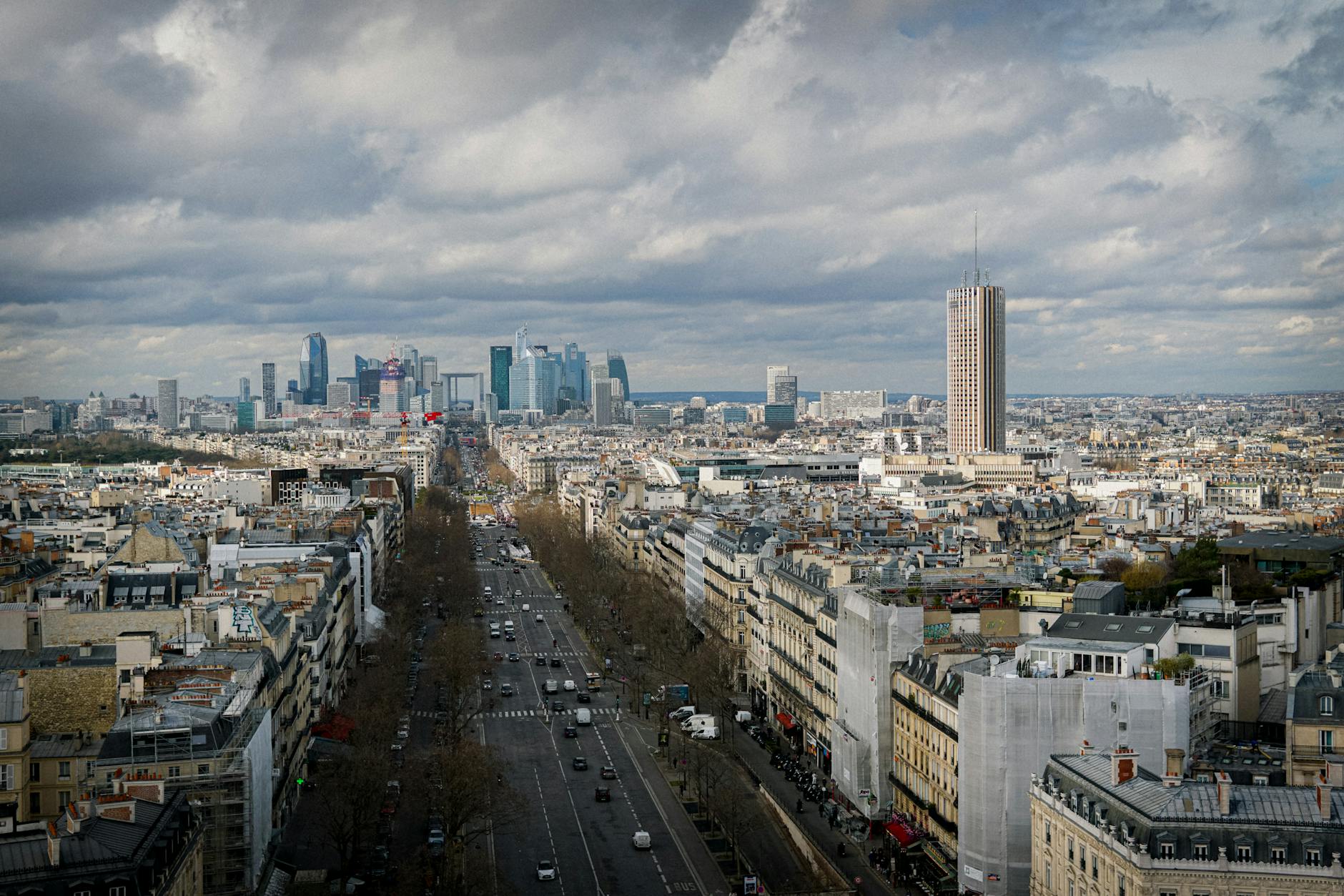 Aerial view of Paris featuring the La Défense skyline under a cloudy sky.