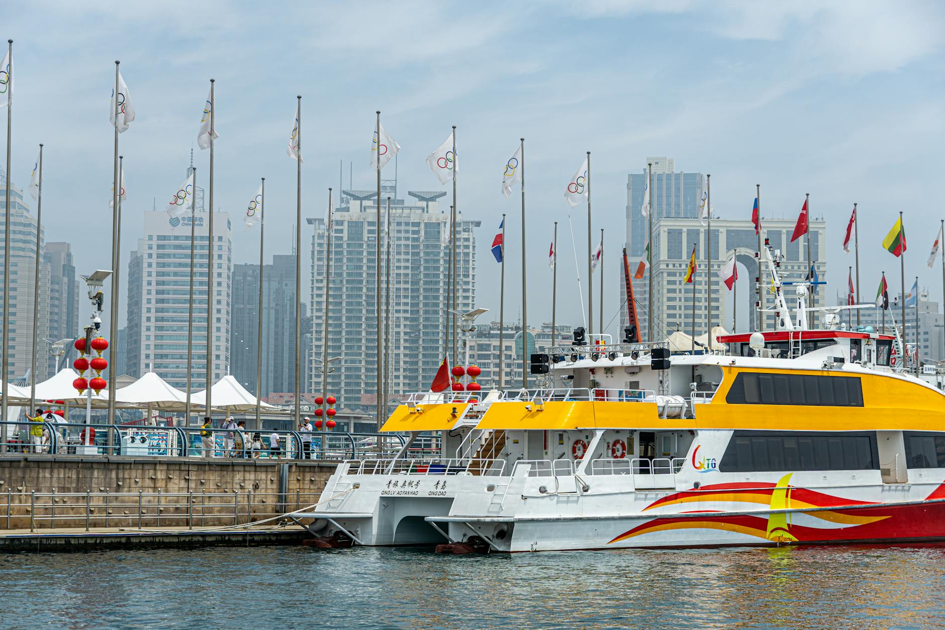 A bright yellow ferry moored in an urban harbor with skyscrapers and flags in the background.