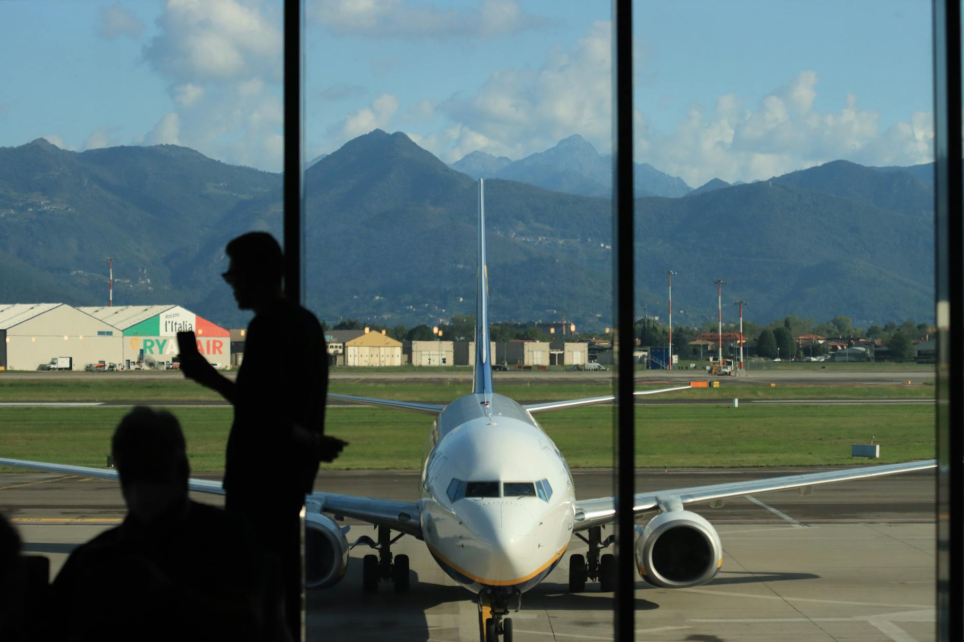 A silhouette of a person at Bergamo airport, overlooking a parked airplane with mountain backdrop.