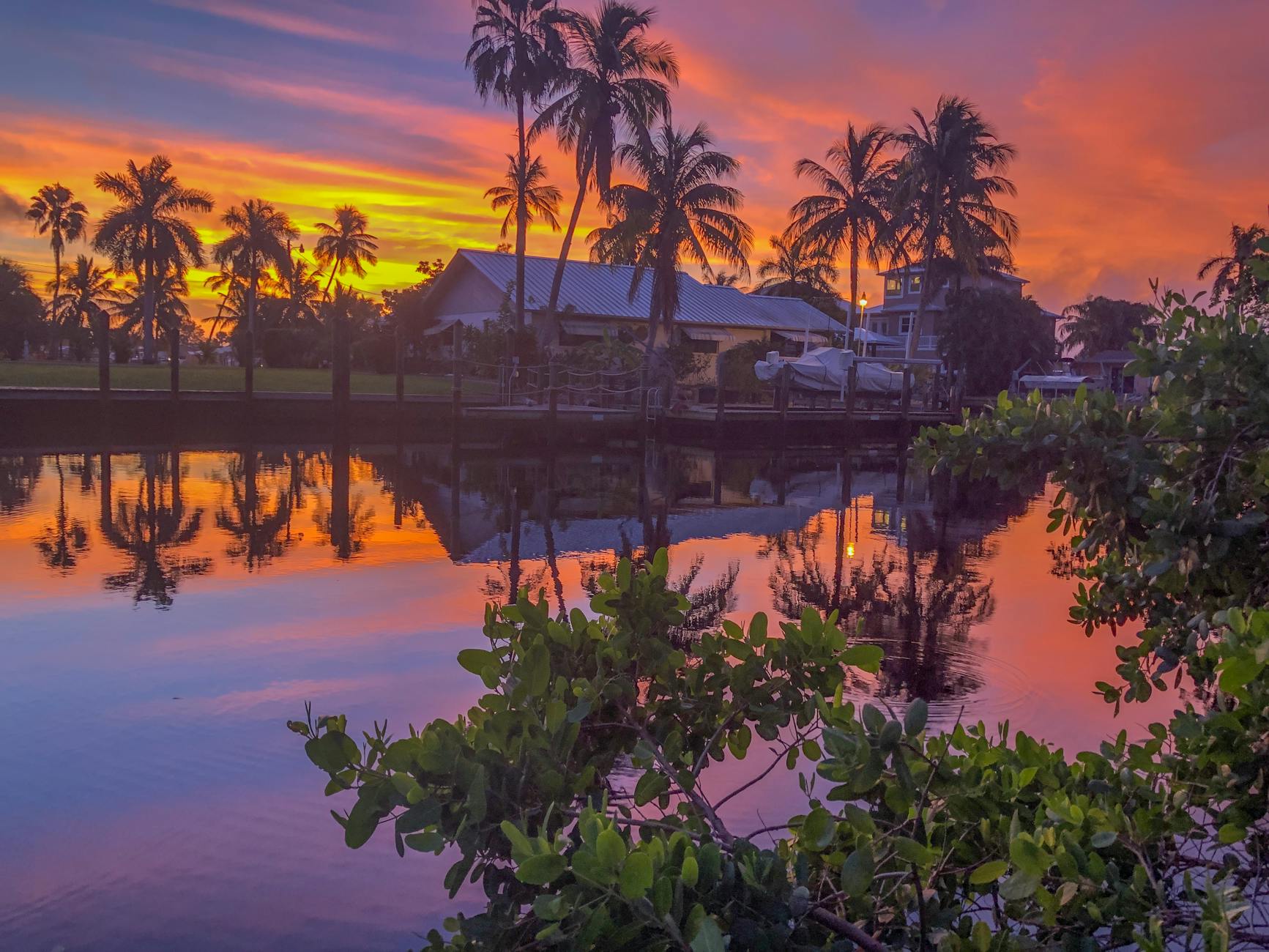 Southwest Florida International Airport (RSW) Fort Myers — Vibrant sunset over a canal in Florida with palm trees and vivid reflections.