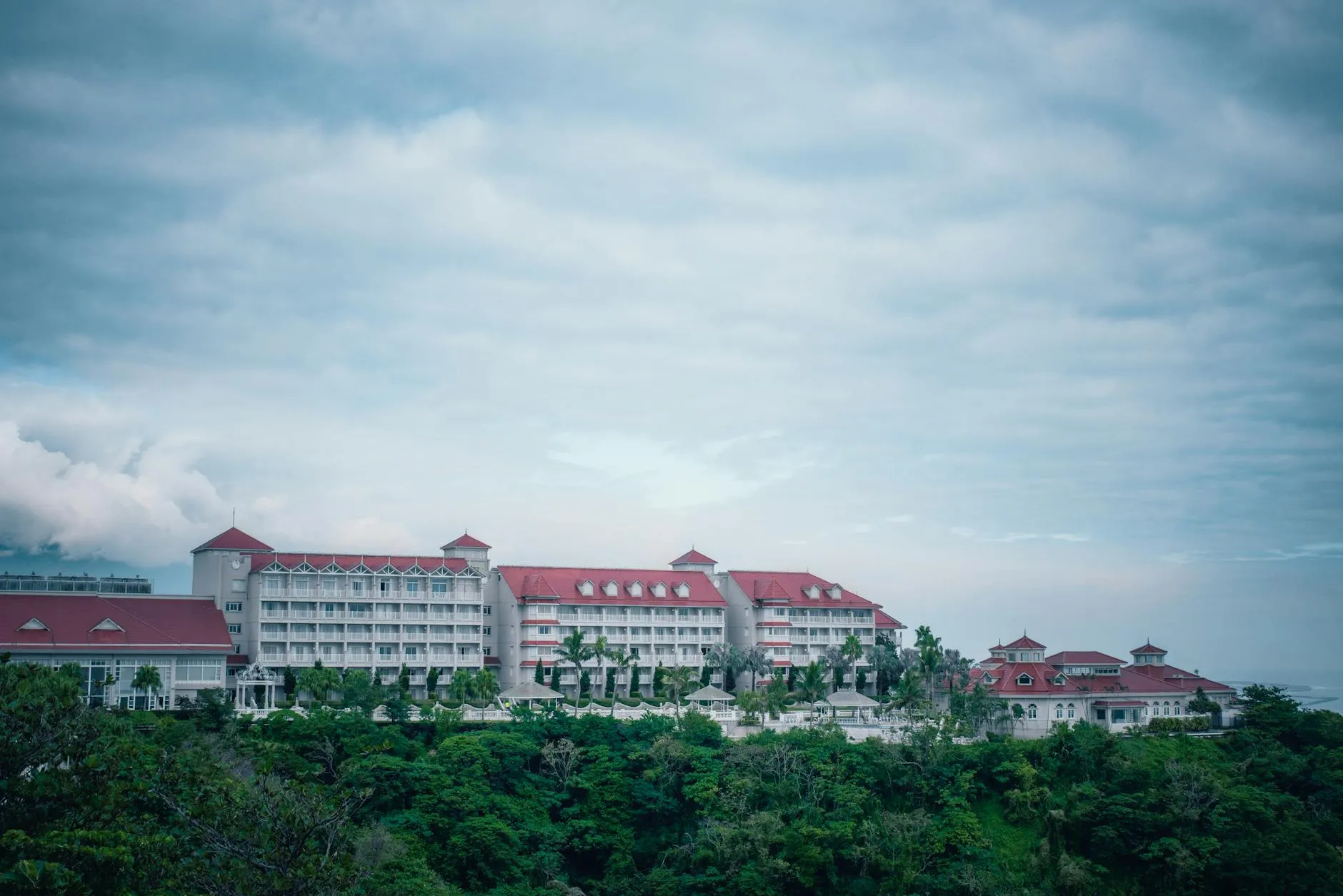 Wide view of a stylish hotel with red roofs amidst lush greenery and cloudy sky in Taiwan.