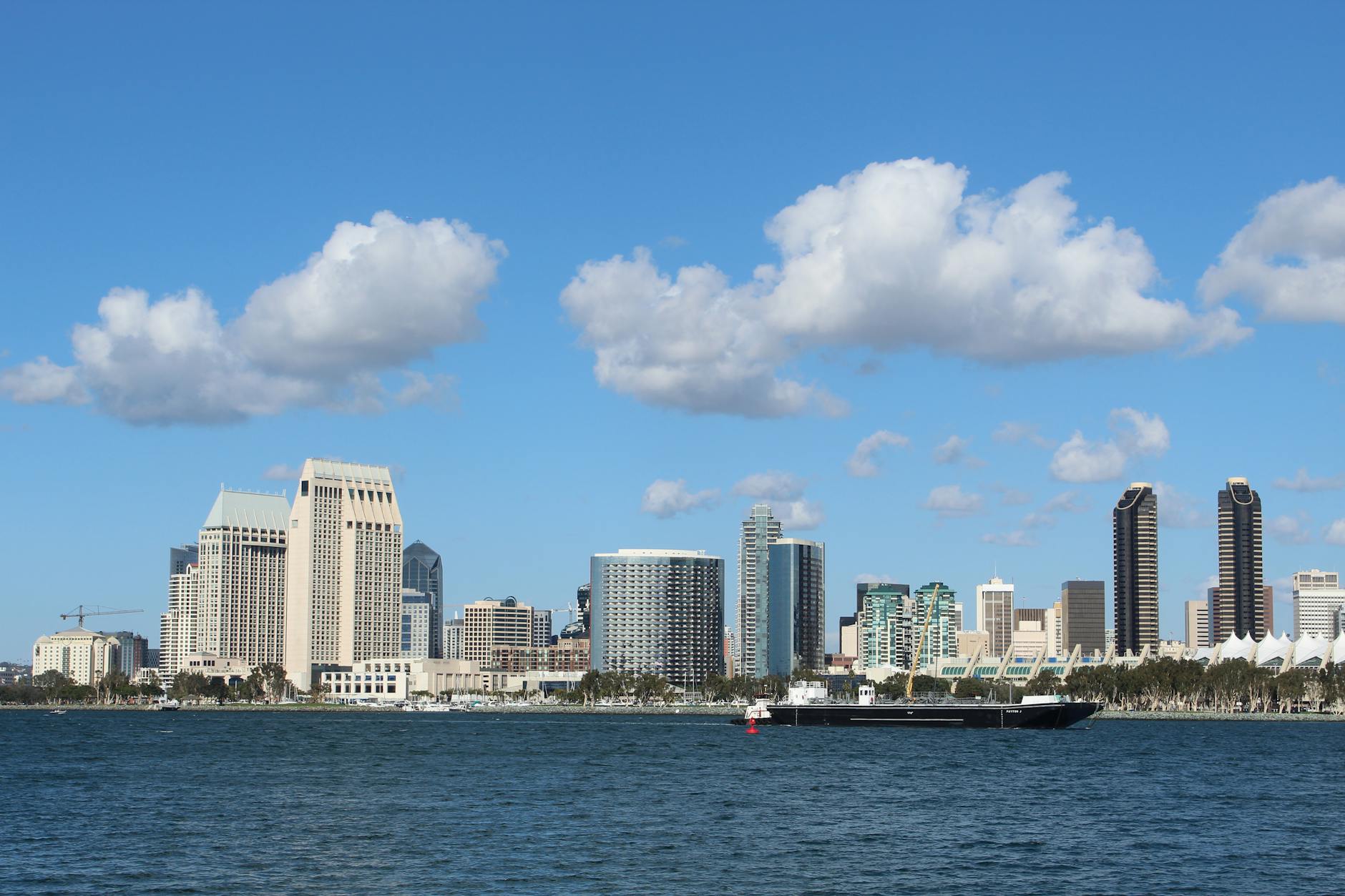 San Diego International Airport (SAN) — View of San Diego skyline with tall buildings and a ship on a bright day.