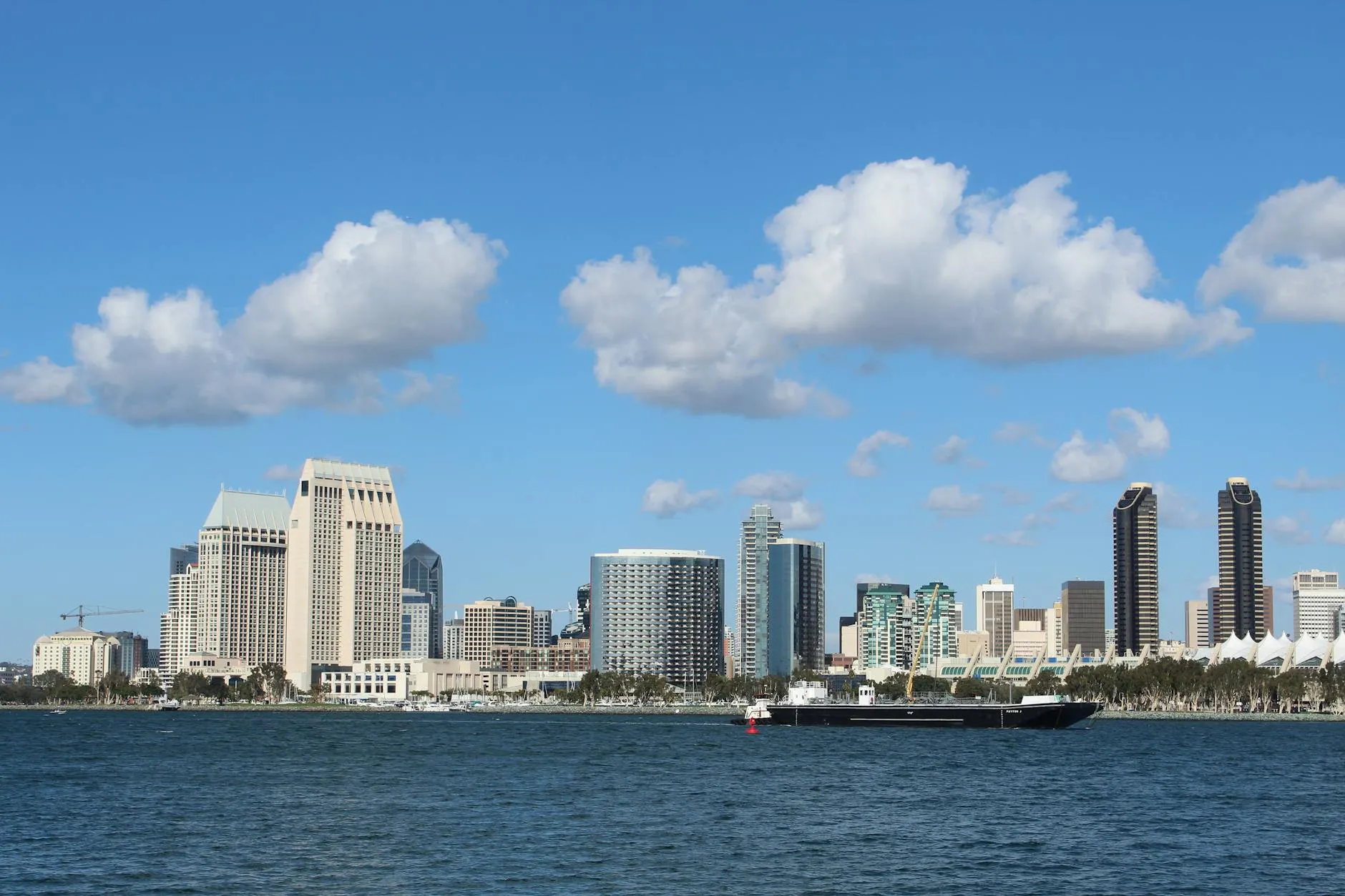 San Diego International Airport (SAN) — View of San Diego skyline with tall buildings and a ship on a bright day.