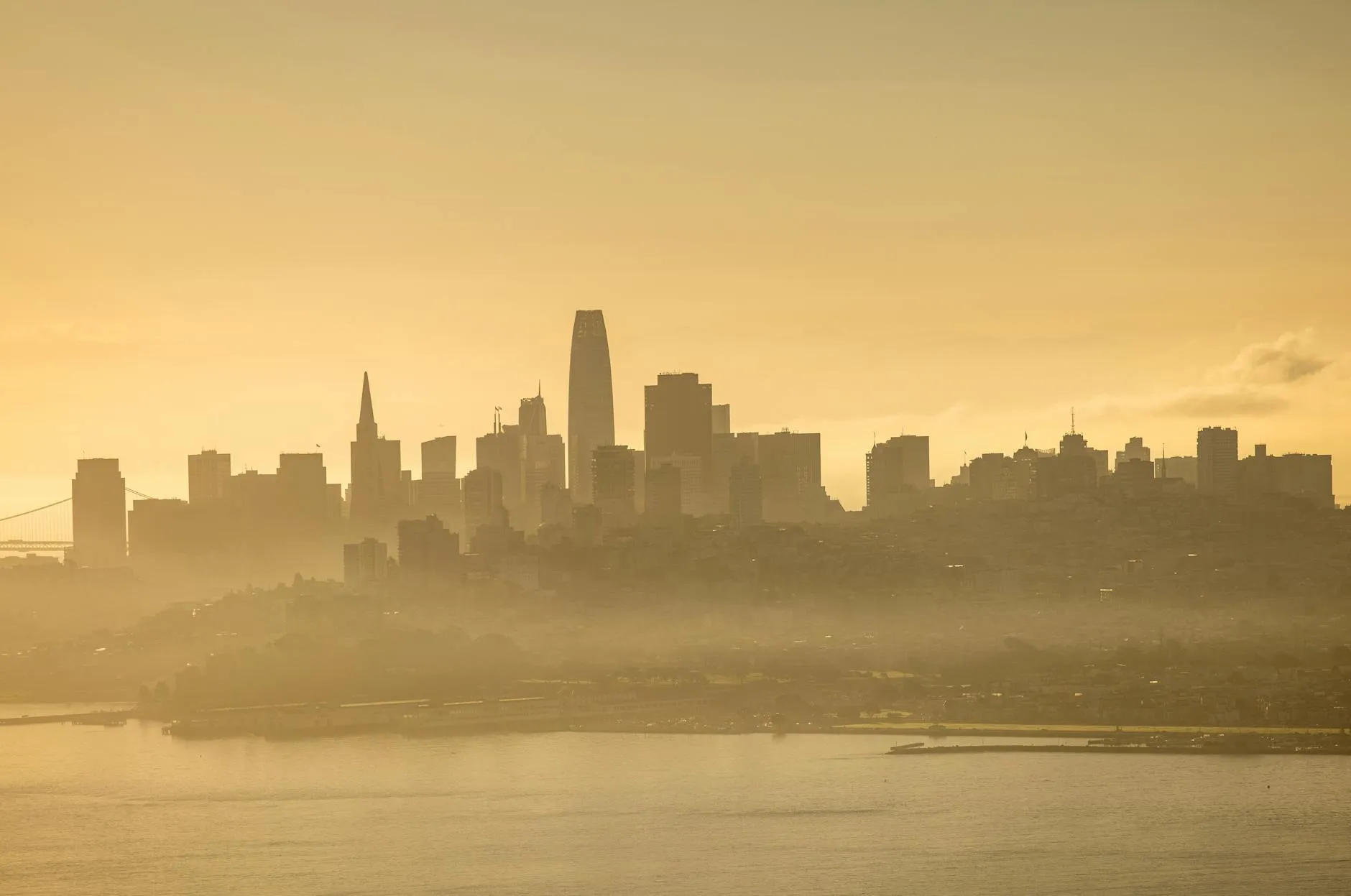 Ethereal view of San Francisco skyline at dawn with golden hues and mist.