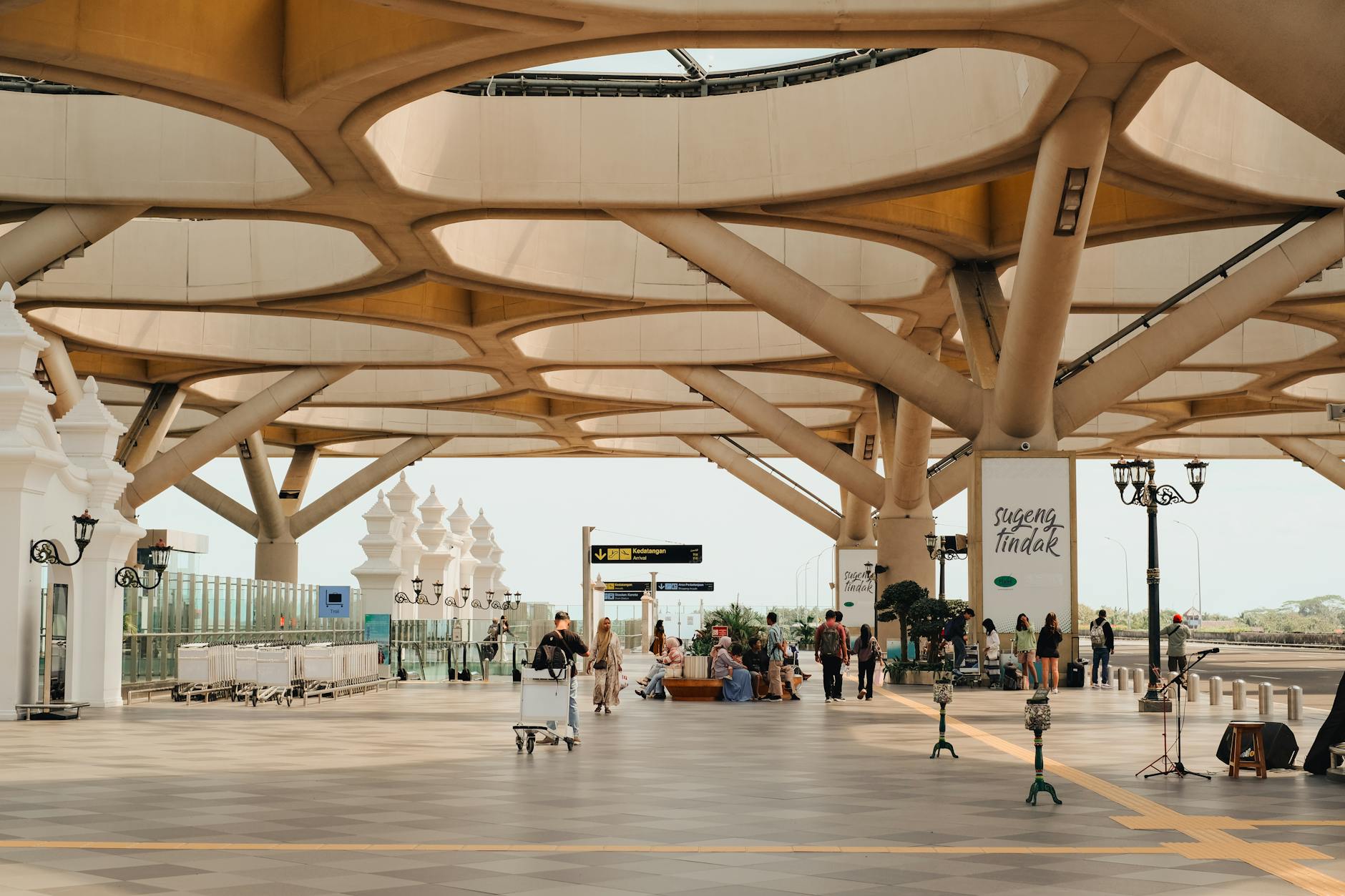 A spacious outdoor station with modern architectural design featuring intricate ceiling patterns and people in transit.