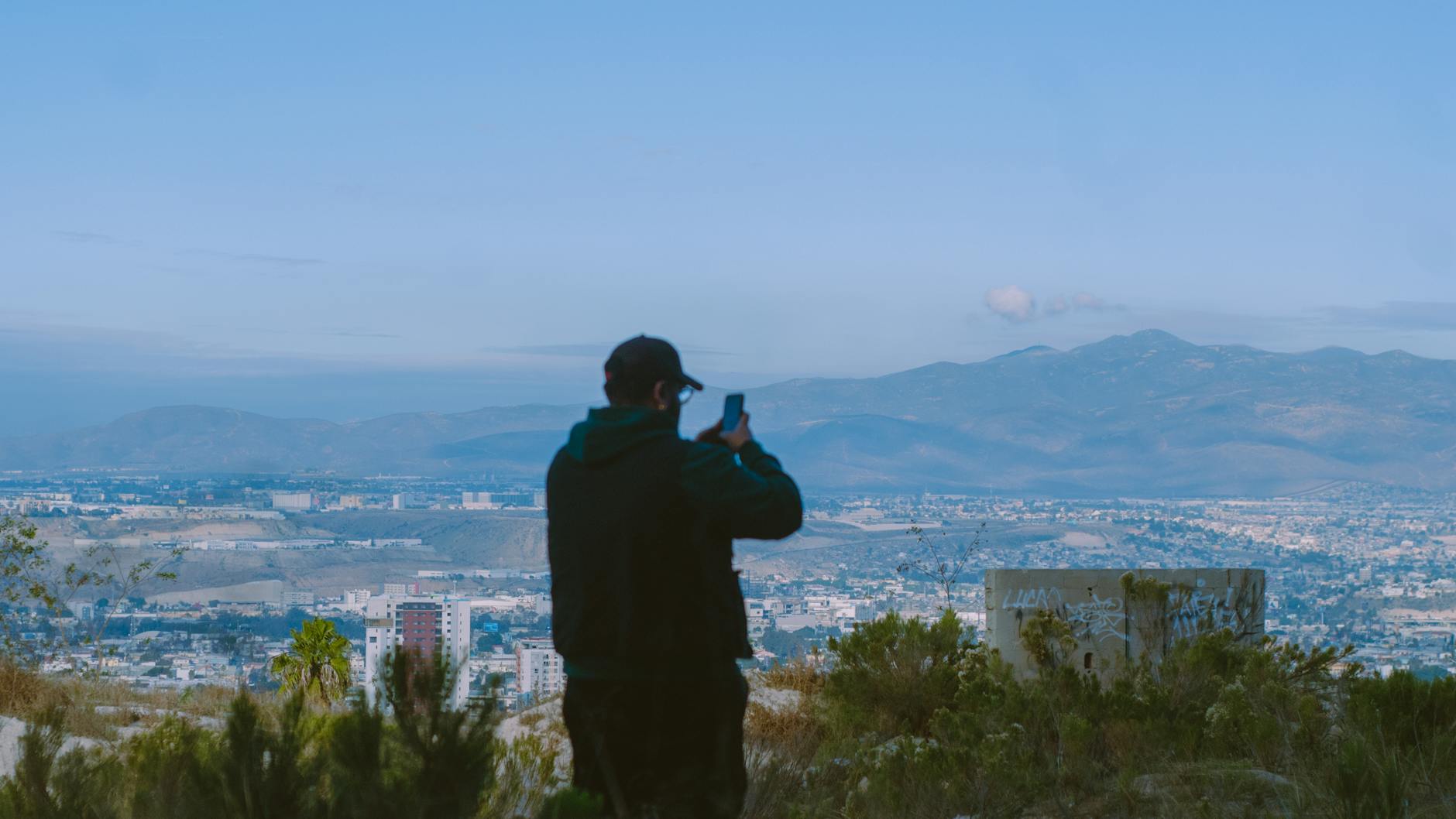Tijuana, Mexico — A man captures a stunning mountain and cityscape view in Tijuana, Mexico, showcasing adventure and exploration.