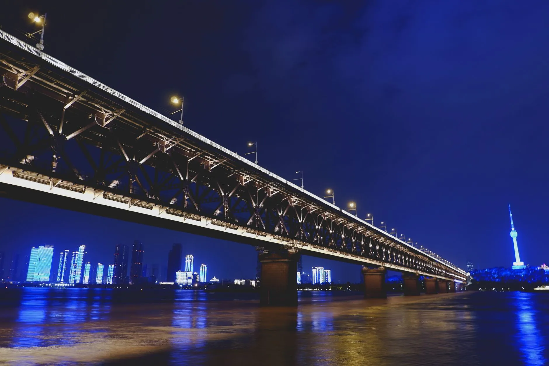 Wuhan, China — Illuminated view of Wuhan's Yangtze River Bridge with city skyline at night.