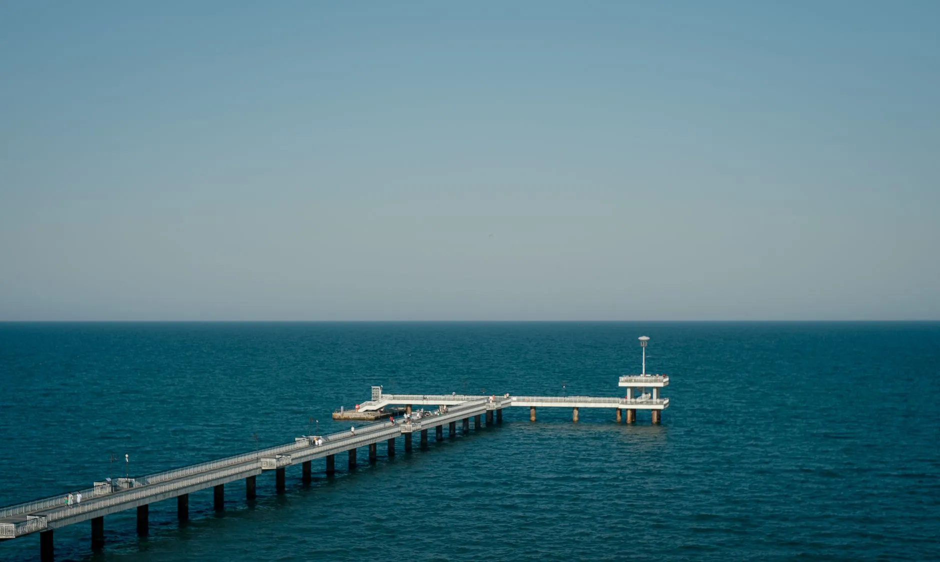 Burgas, Bulgaria — A tranquil view of the Burgas Pier reaching into the blue ocean under a clear sky.