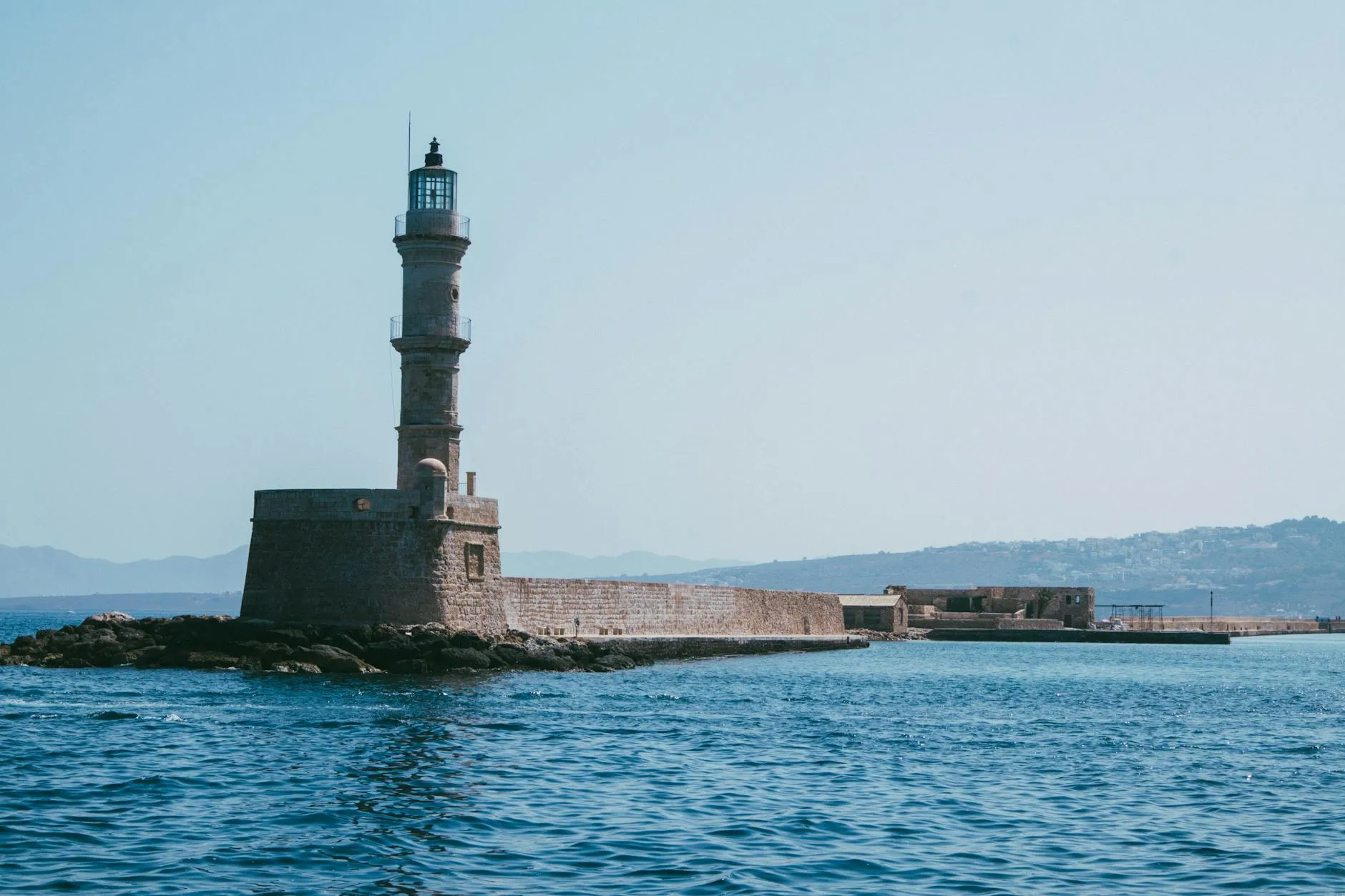 Chania, Crete — View of the iconic Chania Lighthouse and Venetian Harbor in Crete, Greece on a sunny day.