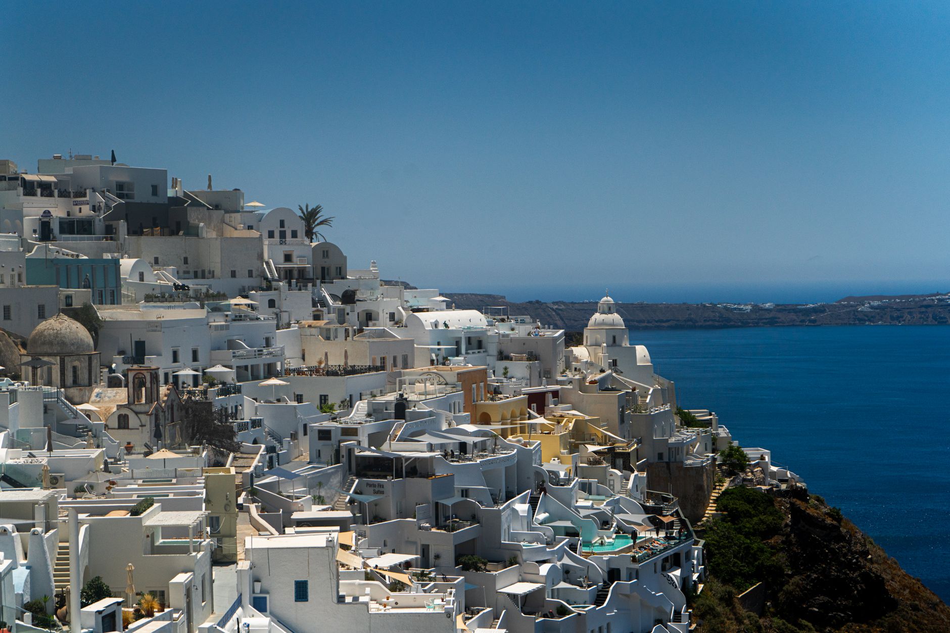 Santorini, Greece — Stunning view of white buildings in Fira, Santorini, Greece against the Aegean Sea under a summer sky.