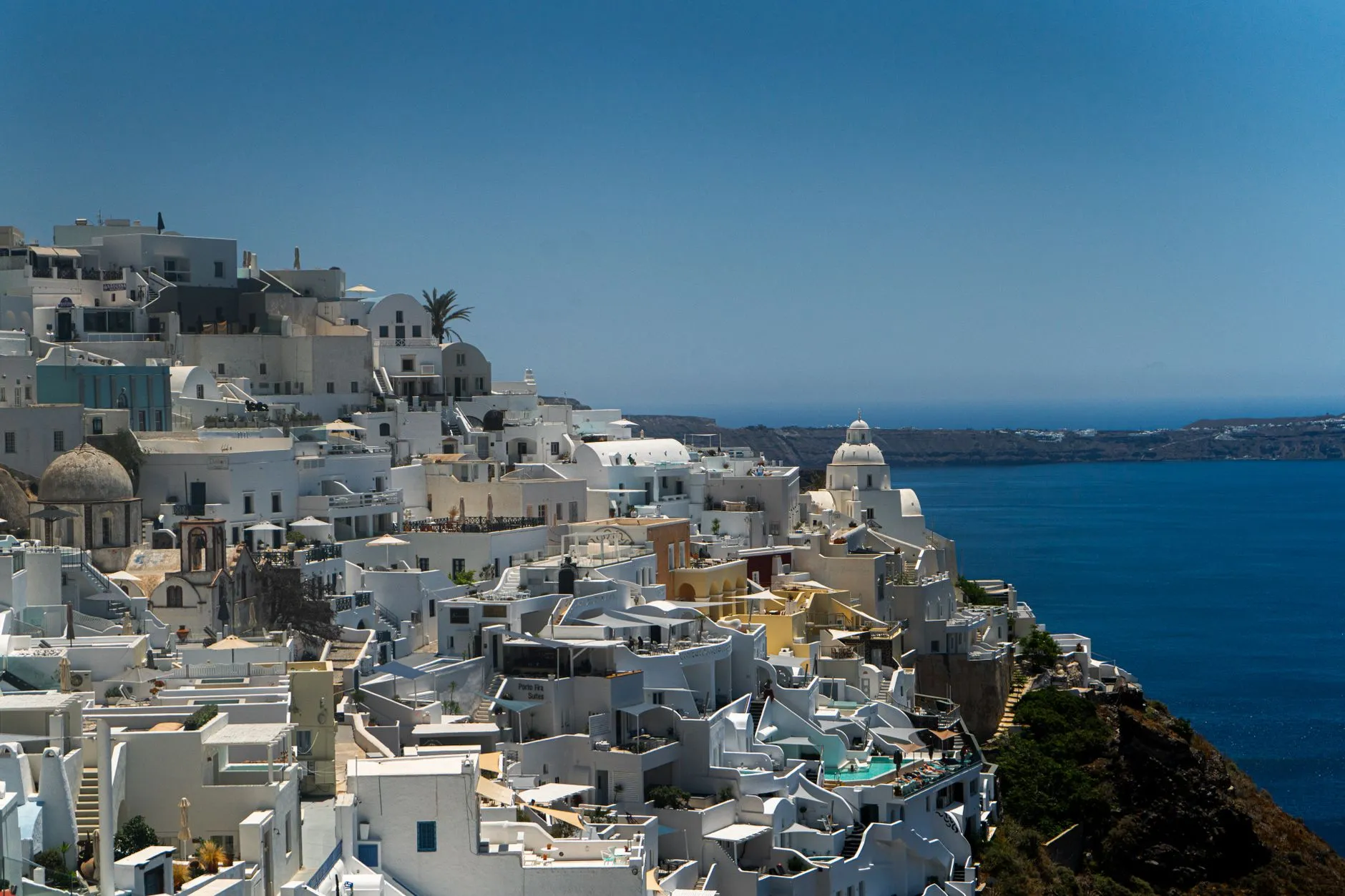 Santorini, Greece — Stunning view of white buildings in Fira, Santorini, Greece against the Aegean Sea under a summer sky.