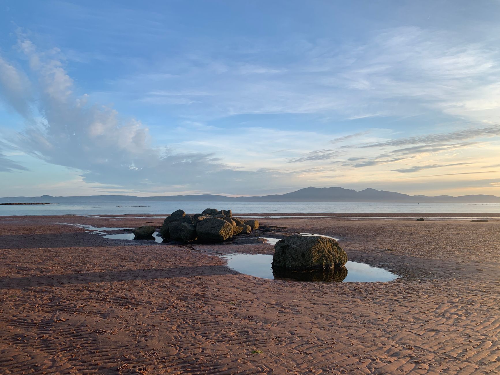 Prestwick, Scotland — Peaceful beach scene with rocks and puddles in North Ayrshire, Scotland, under a vibrant evening sky.