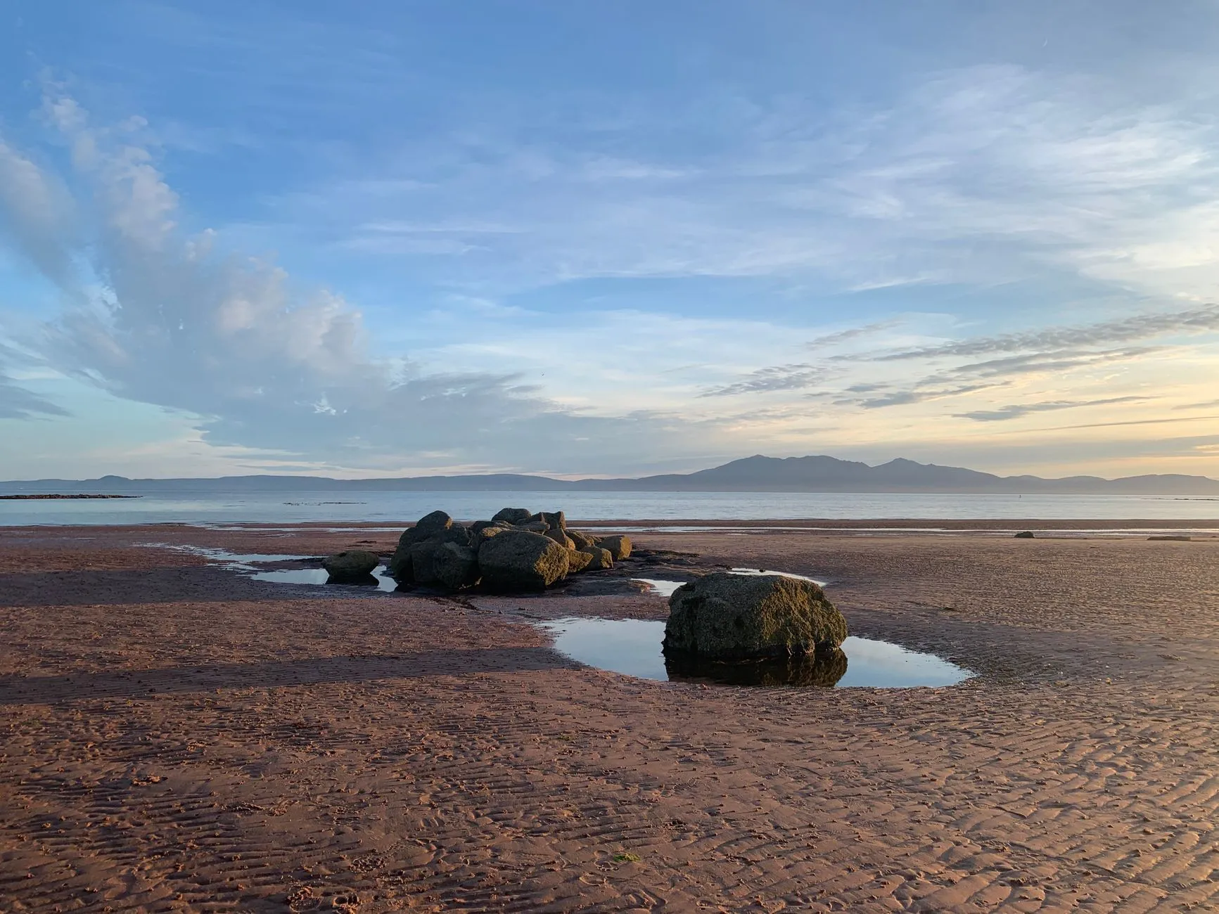 Prestwick, Scotland — Peaceful beach scene with rocks and puddles in North Ayrshire, Scotland, under a vibrant evening sky.
