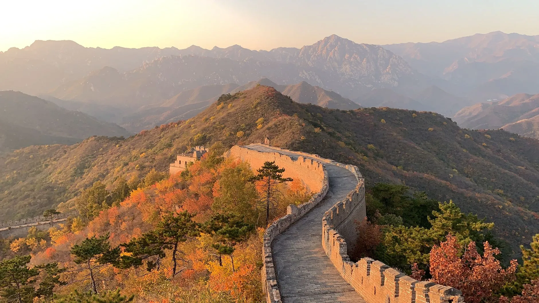 China — Great Wall of China going through hill with green trees with mountains behind on sunny day