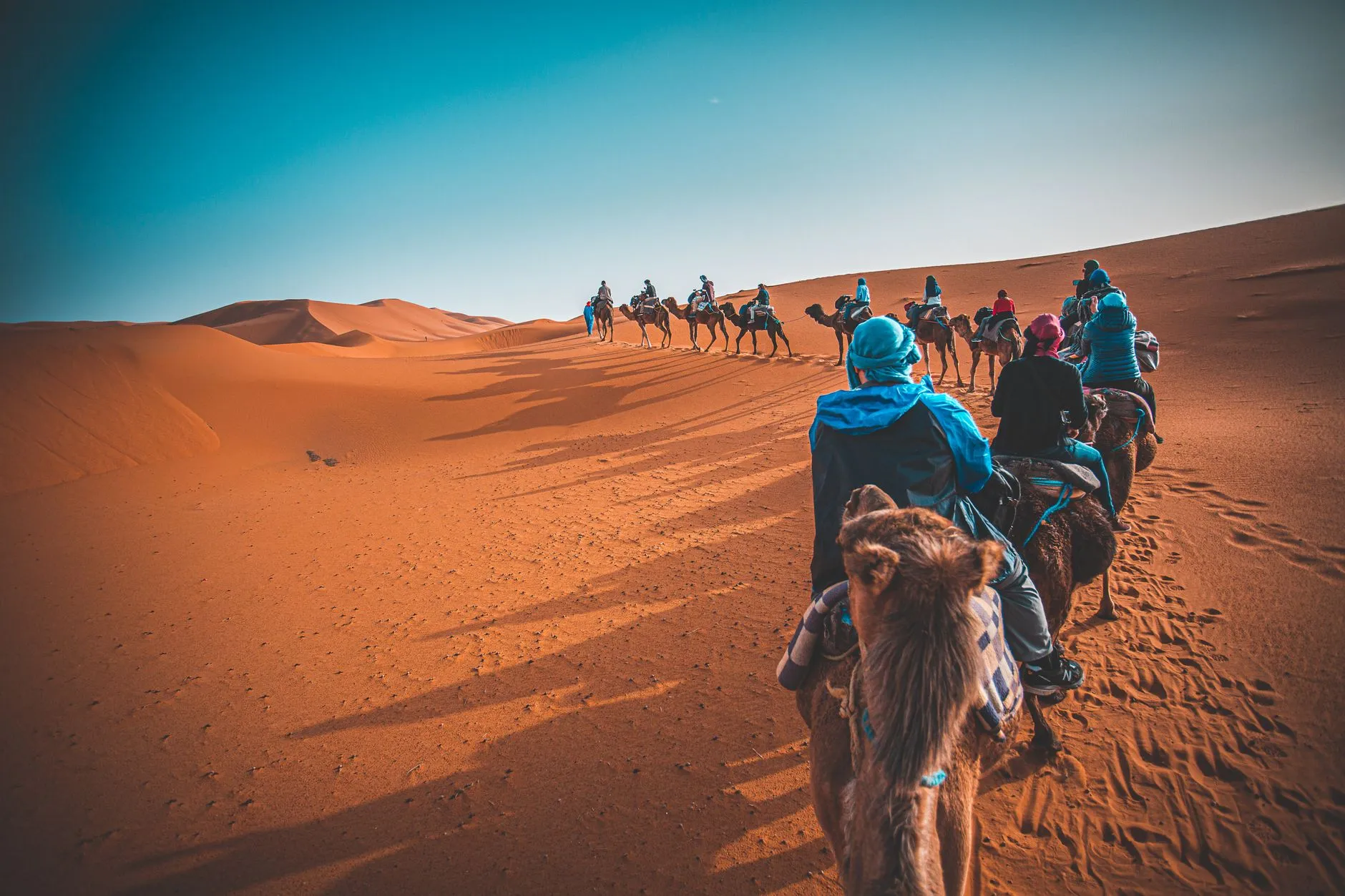 Morocco — A group of people riding camels through the Sahara desert in Merzouga, Morocco at sunset.
