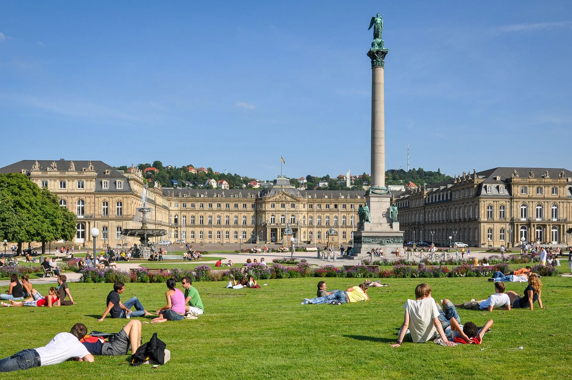 Stuttgart, Germany — People relaxing on the grass at Schlossplatz, Stuttgart, under a sunny sky with Neues Schloss in the background.