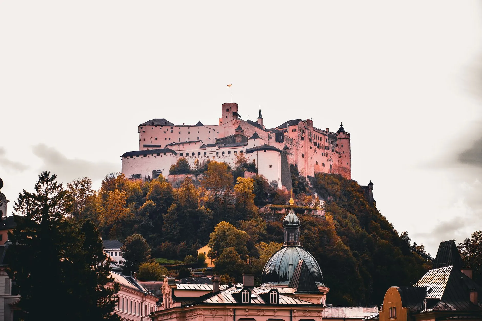 Salzburg, Austria — View of the Hohensalzburg Fortress atop a hill surrounded by vibrant autumn foliage in Salzburg, Austria.