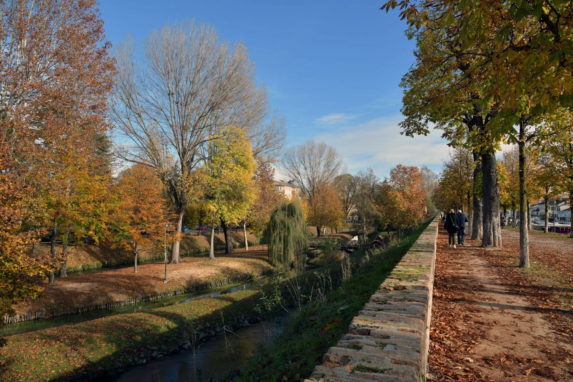 Treviso, Veneto, Italy — Enjoy a scenic autumn walk along a picturesque canal in Treviso, Italy with vibrant foliage.