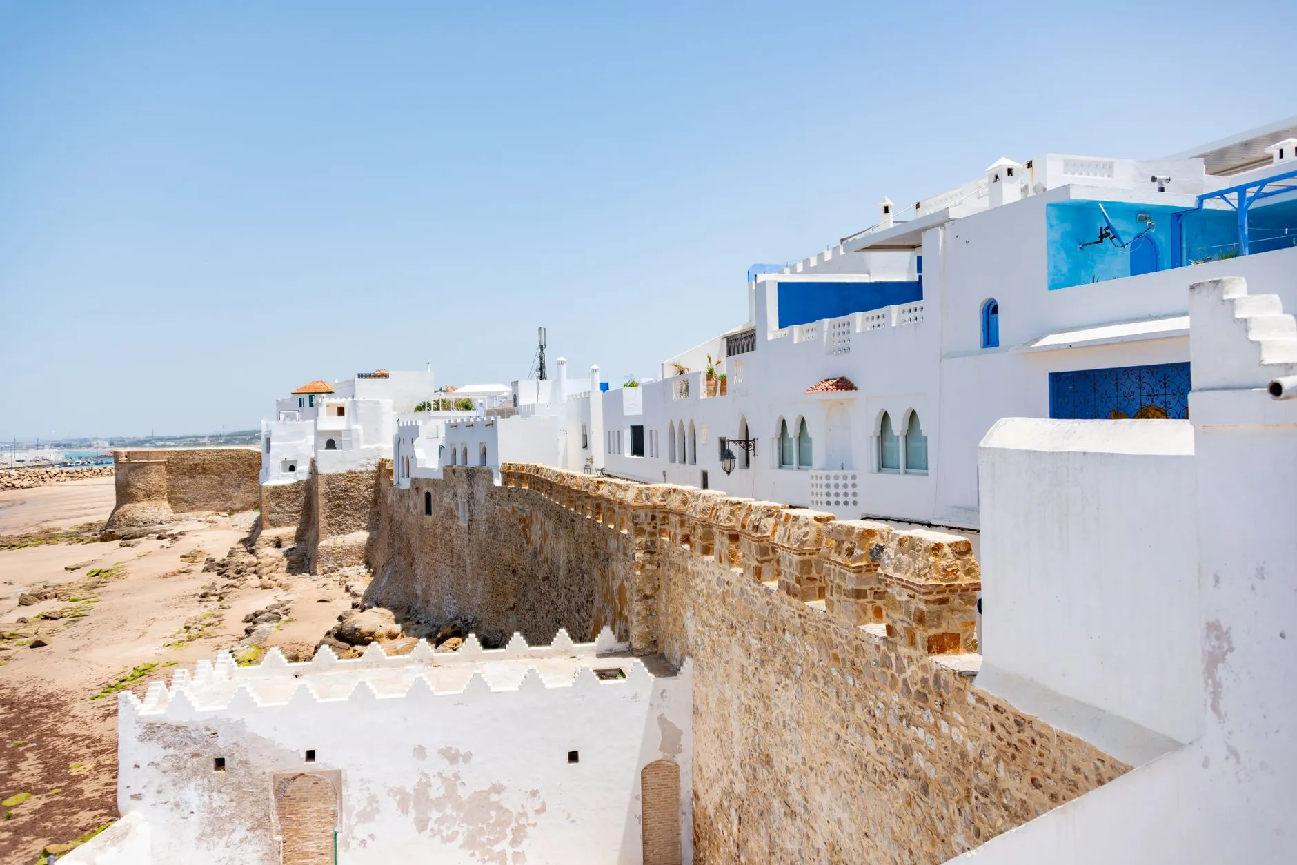 Tétouan, Morocco — A view of a whitewashed medina with an ancient seaside fortress under a clear blue sky in Morocco.