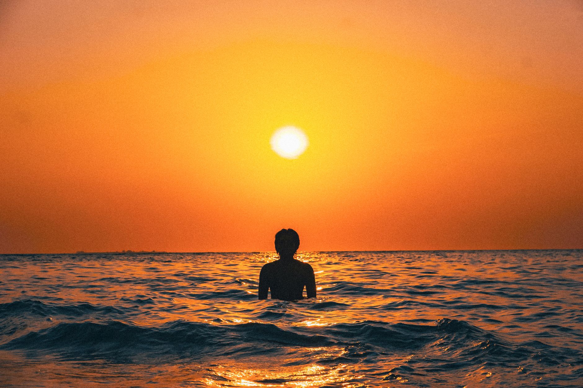 Makassar, Indonesia — A silhouette of an individual wading in the ocean during a vibrant sunset in Makassar, Indonesia.