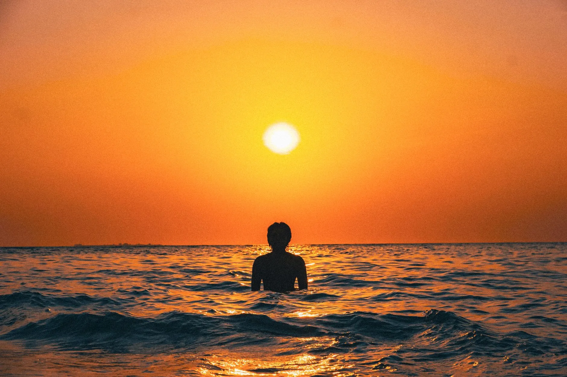 Makassar, Indonesia — A silhouette of an individual wading in the ocean during a vibrant sunset in Makassar, Indonesia.